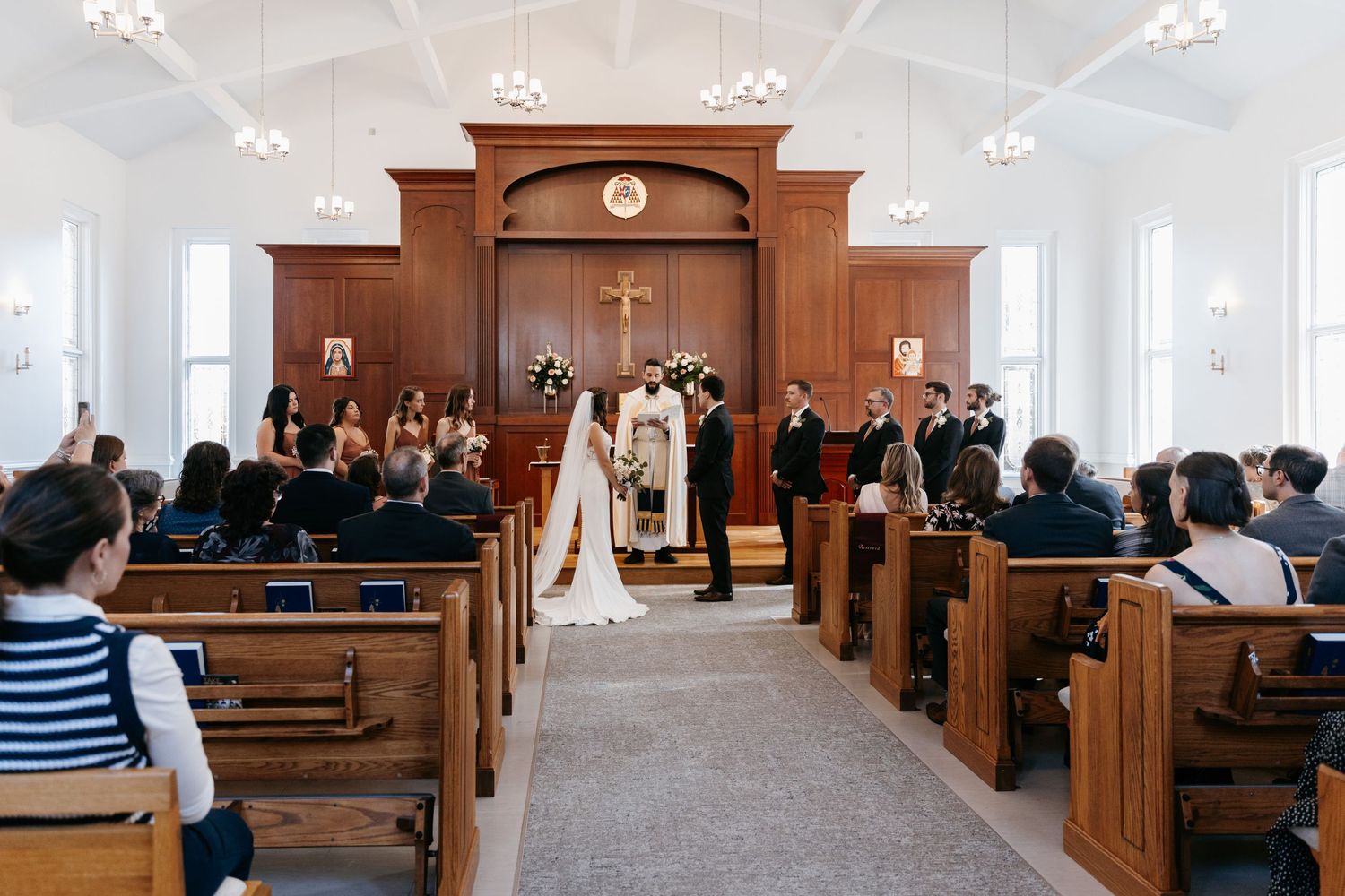 Interior church wedding ceremony with wooden pews and white walls.