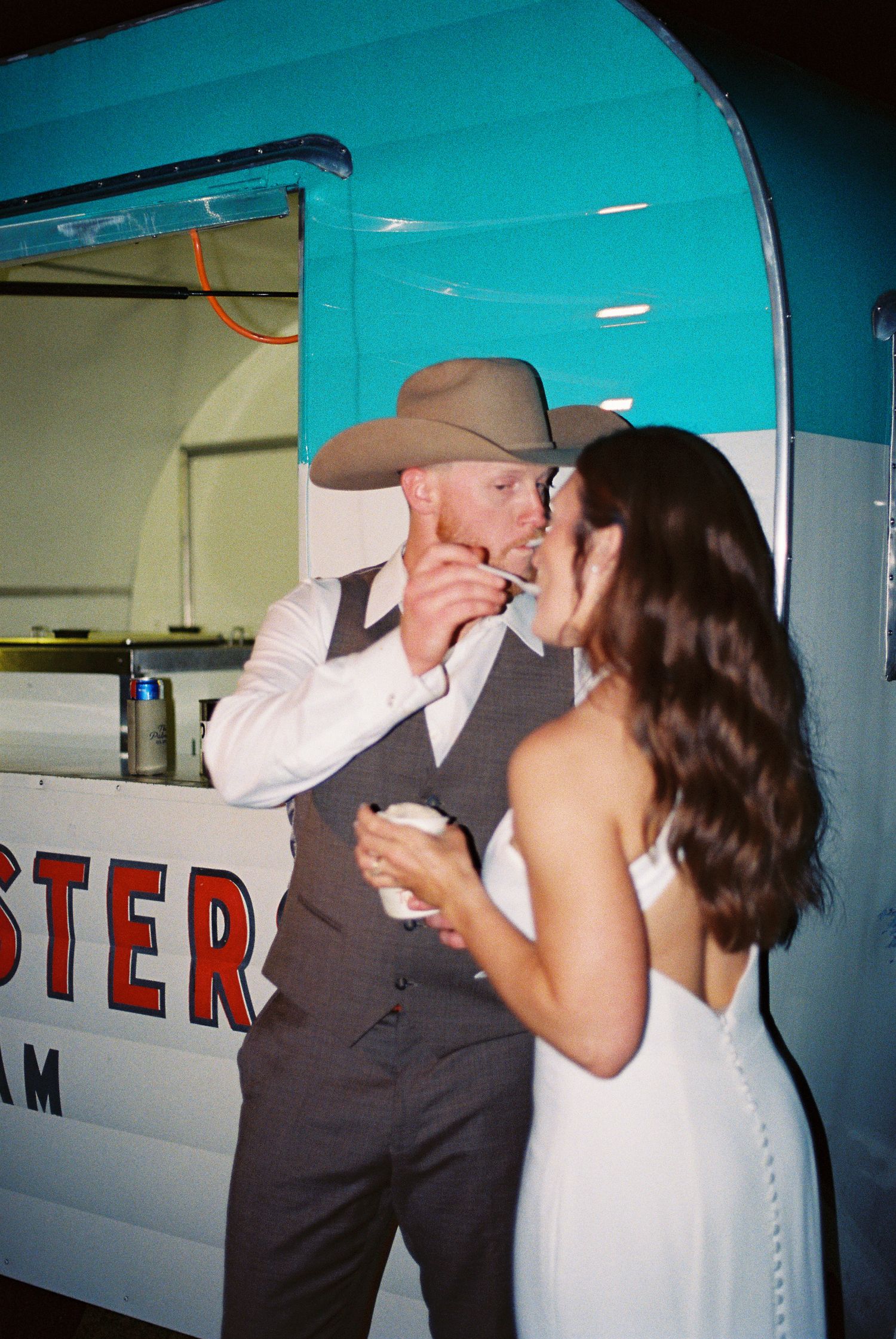 Bride and groom sharing a sweet moment at an ice cream food truck, groom wearing a cowboy hat and vest.