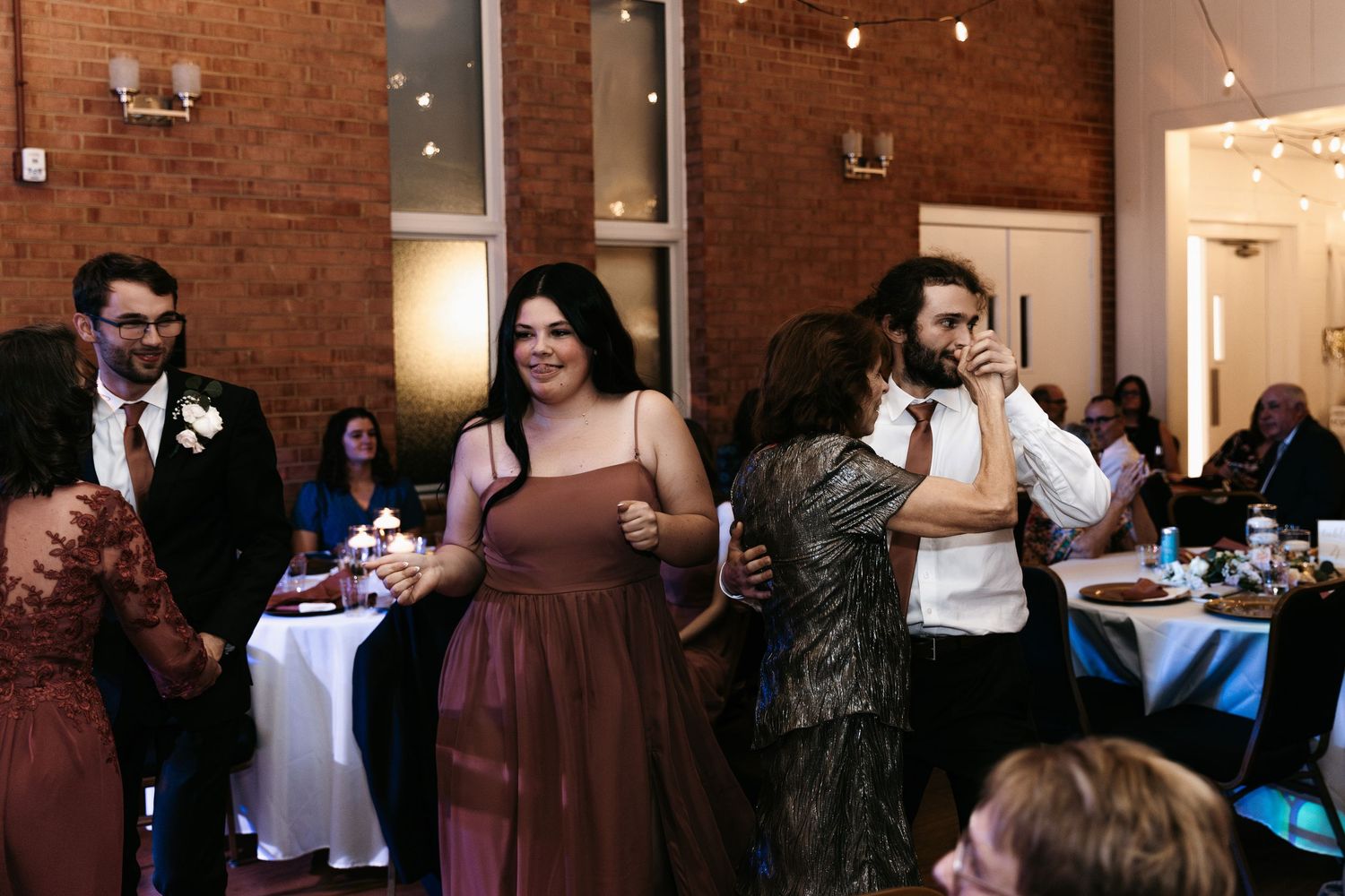 Wedding guests mingling and celebrating in a rustic brick-walled reception space.