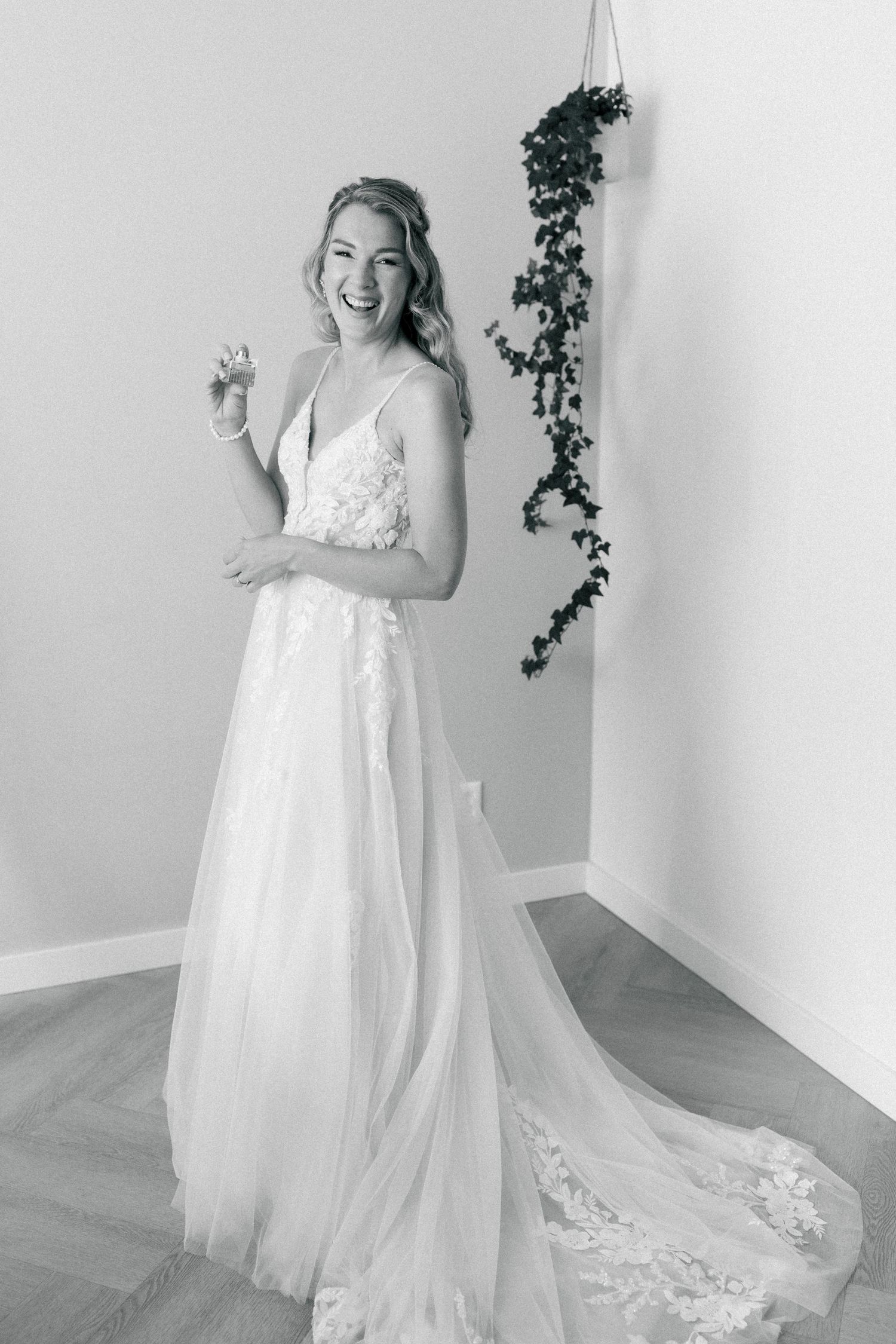 A bride in a flowing white lace wedding gown twirls and dances joyfully in a bright room with ivy decor.