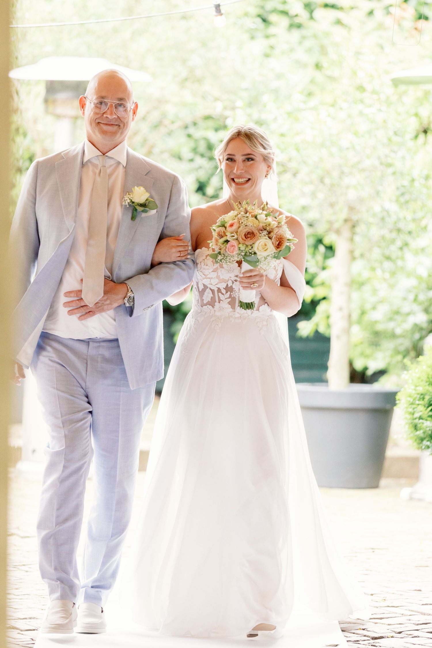 Three ring bearers in light gray suits walk down an outdoor aisle at a wedding ceremony.