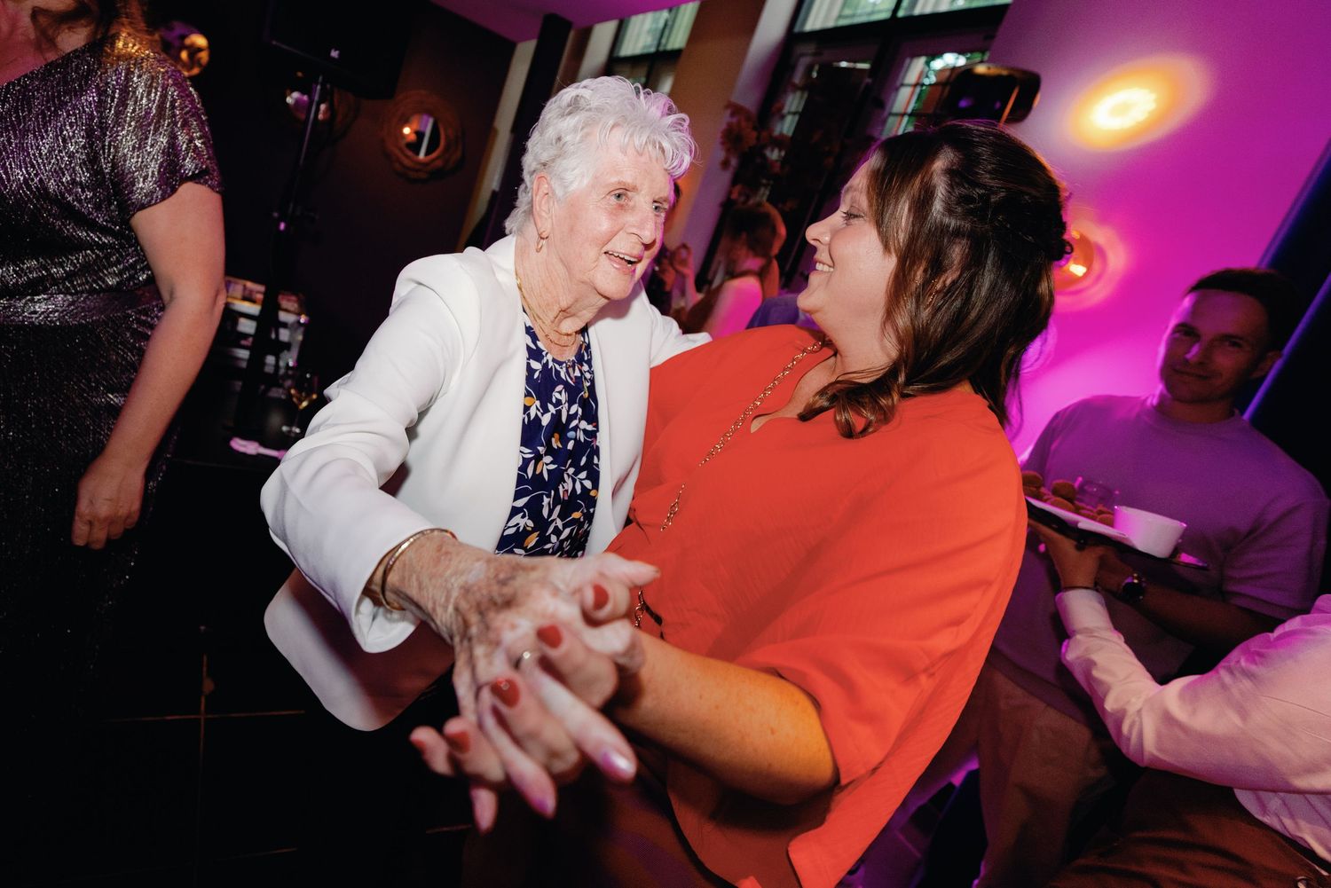 People dancing and socializing at a lively party with colorful purple and red lighting effects.