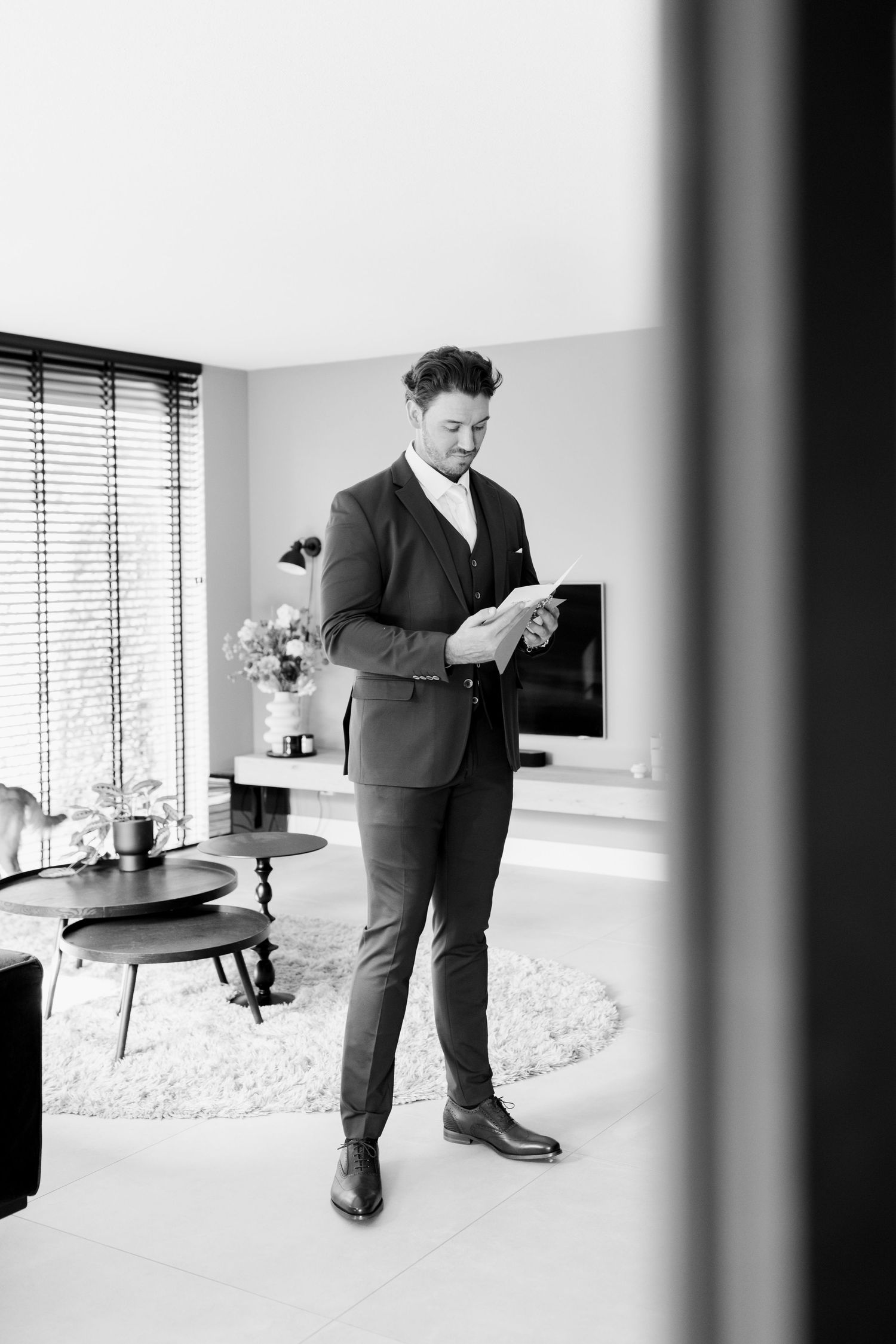 Black and white photo series showing person in suit adjusting their shoes and socks against minimalist interior.