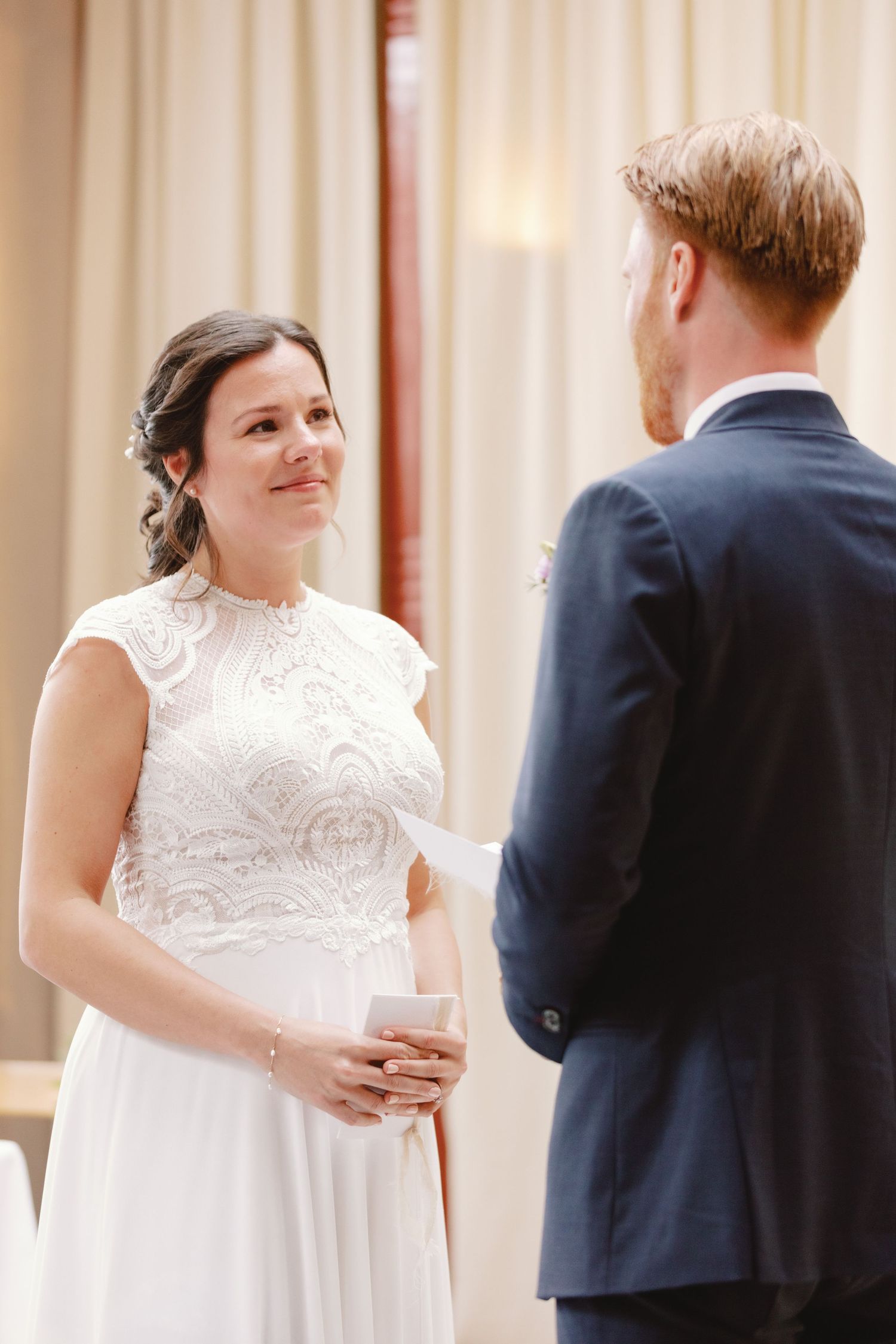 A bride in a white lace dress and groom in navy suit share intimate moments during their wedding ceremony.