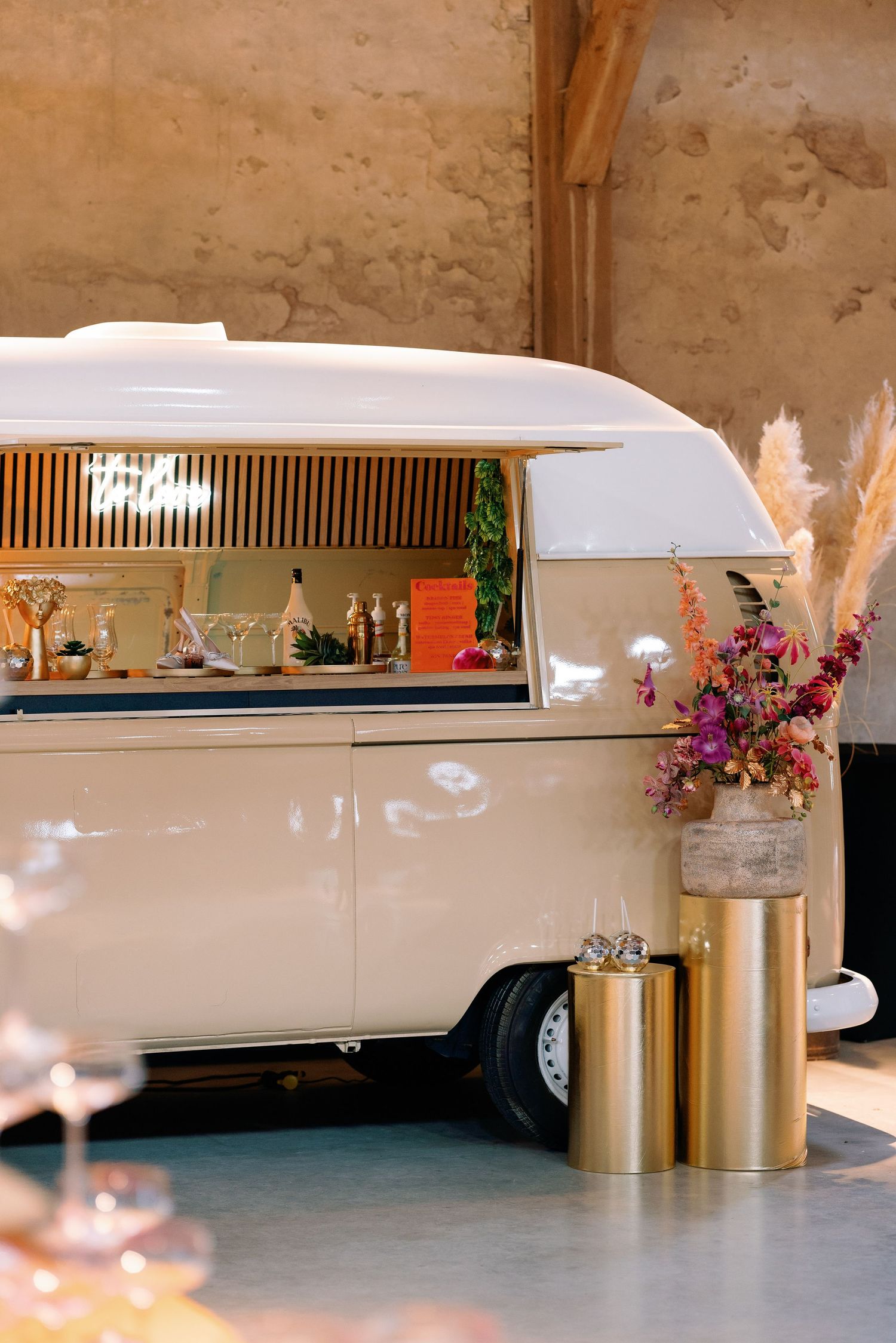 A vintage white caravan bar with floral decorations and a gold vase featuring pampas grass and pink flowers.