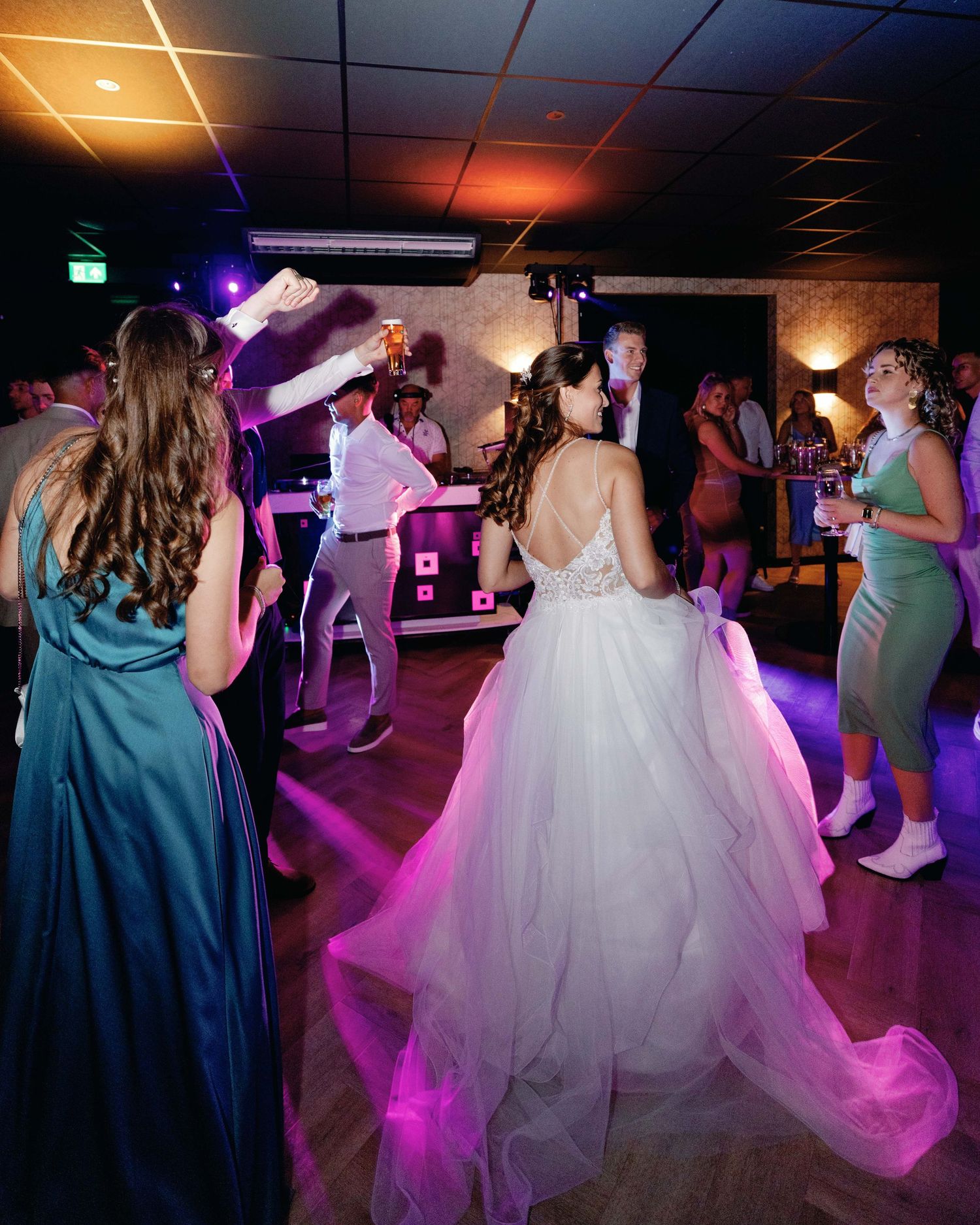 Wedding guests dance under colorful lights while a DJ performs in the background.