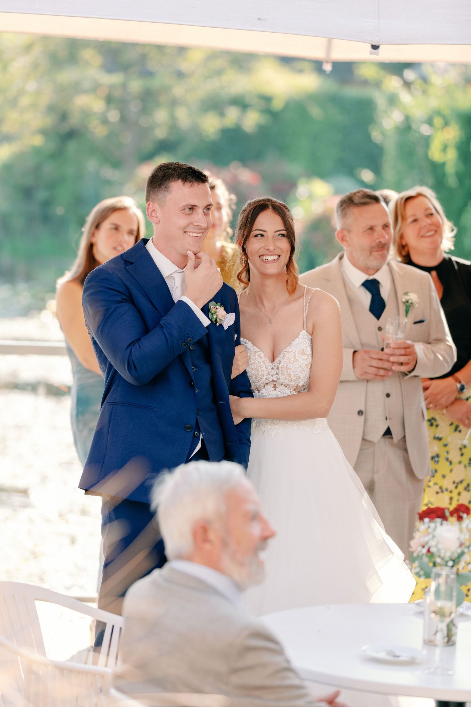 Wedding party celebrates during reception under white tent with floral decorations.