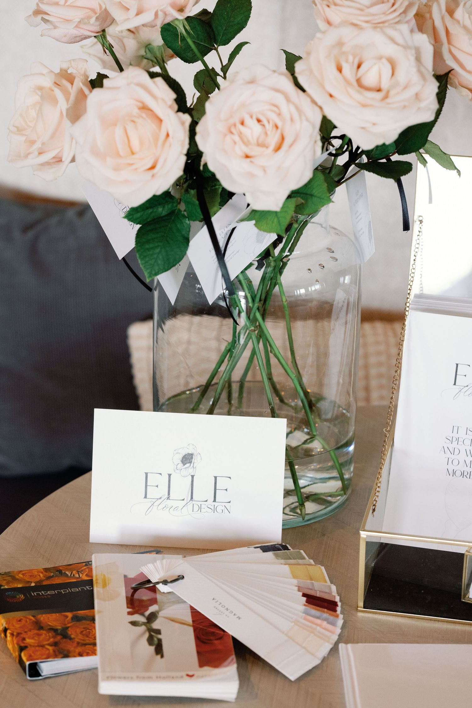 Business cards and branding materials displayed with pale pink roses in glass vases.