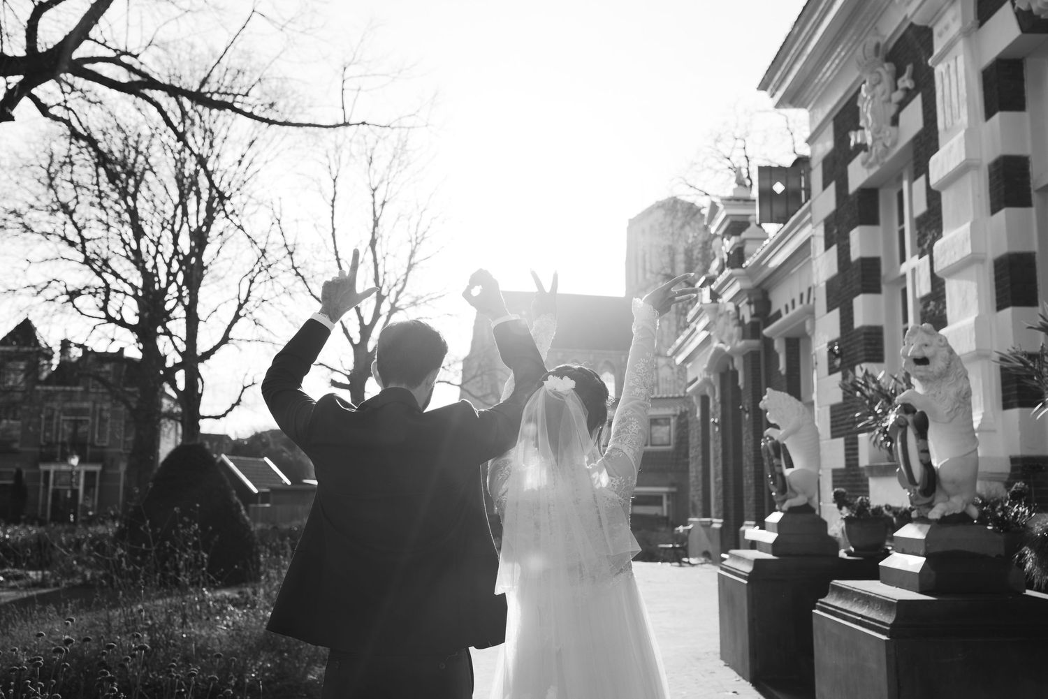 A silhouetted couple embraces during a backlit sunset wedding photo session with trees and buildings in the background.