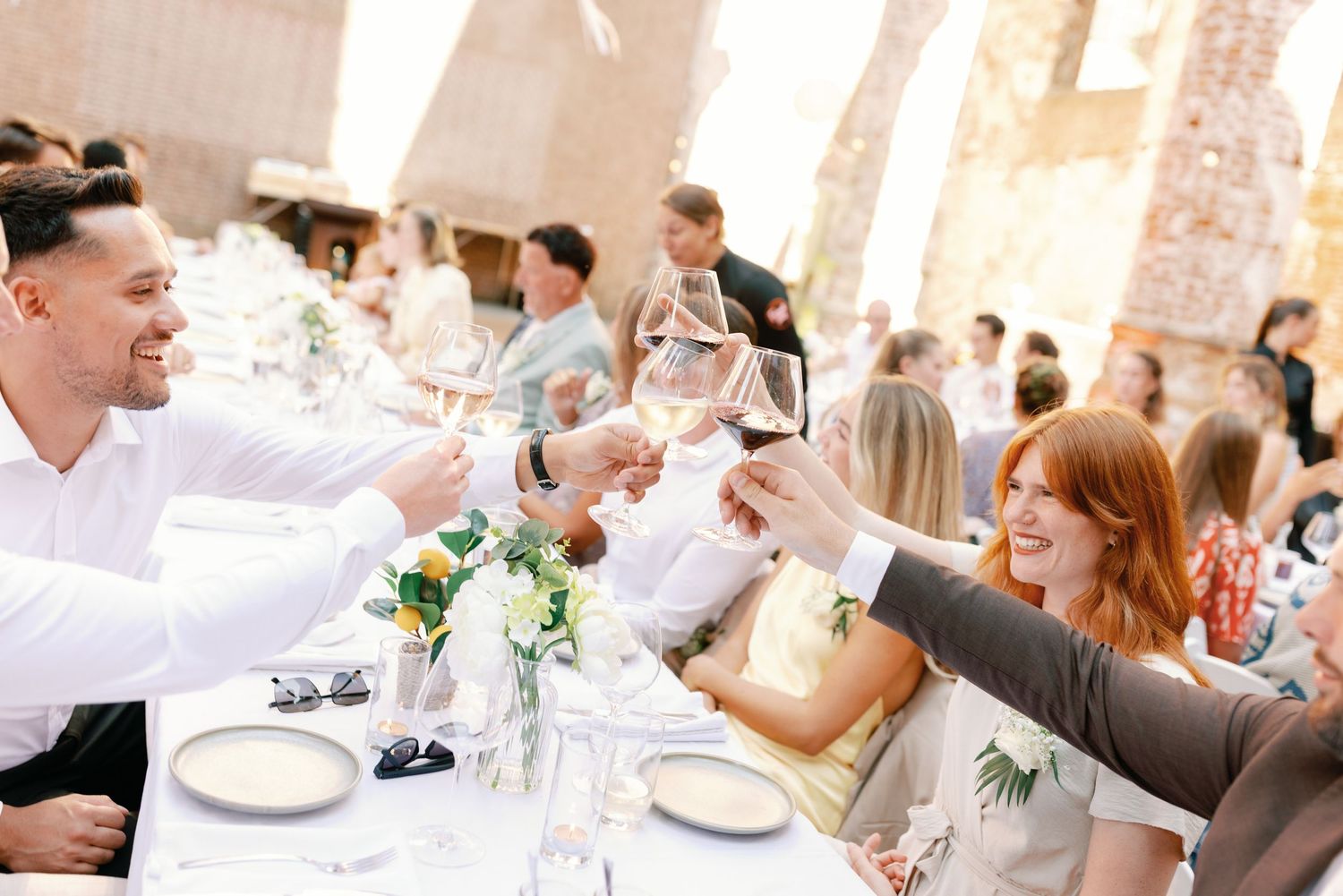 Wedding guests share joyful laughter and conversation during an elegant reception dinner at a bright indoor venue.