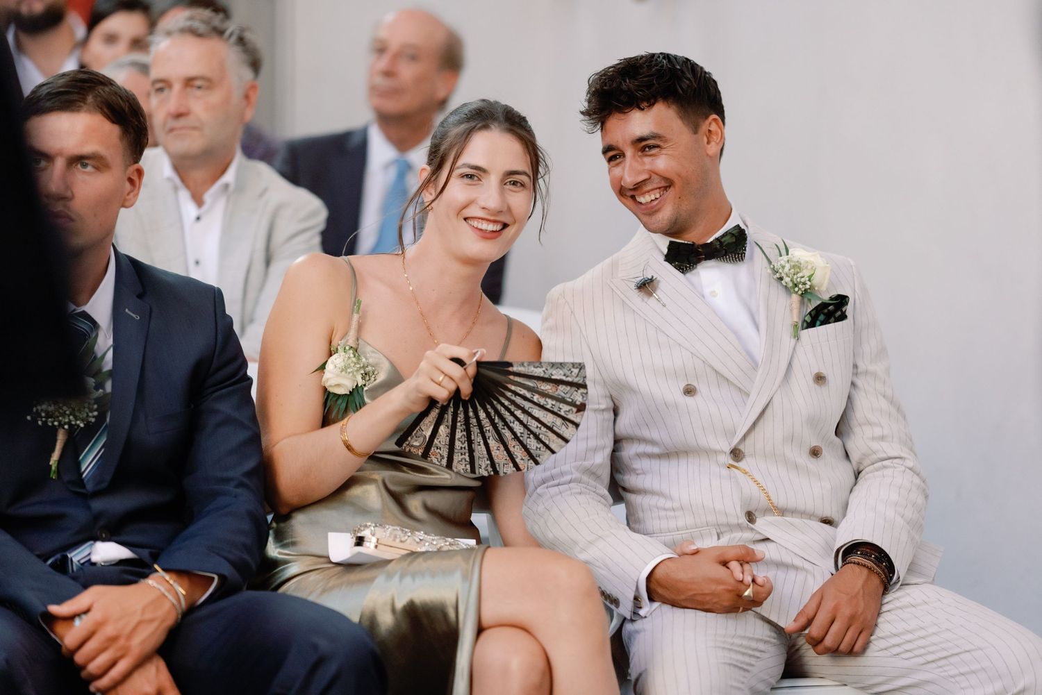 Wedding guests share candid laughter during an outdoor celebration with white and natural decor elements.