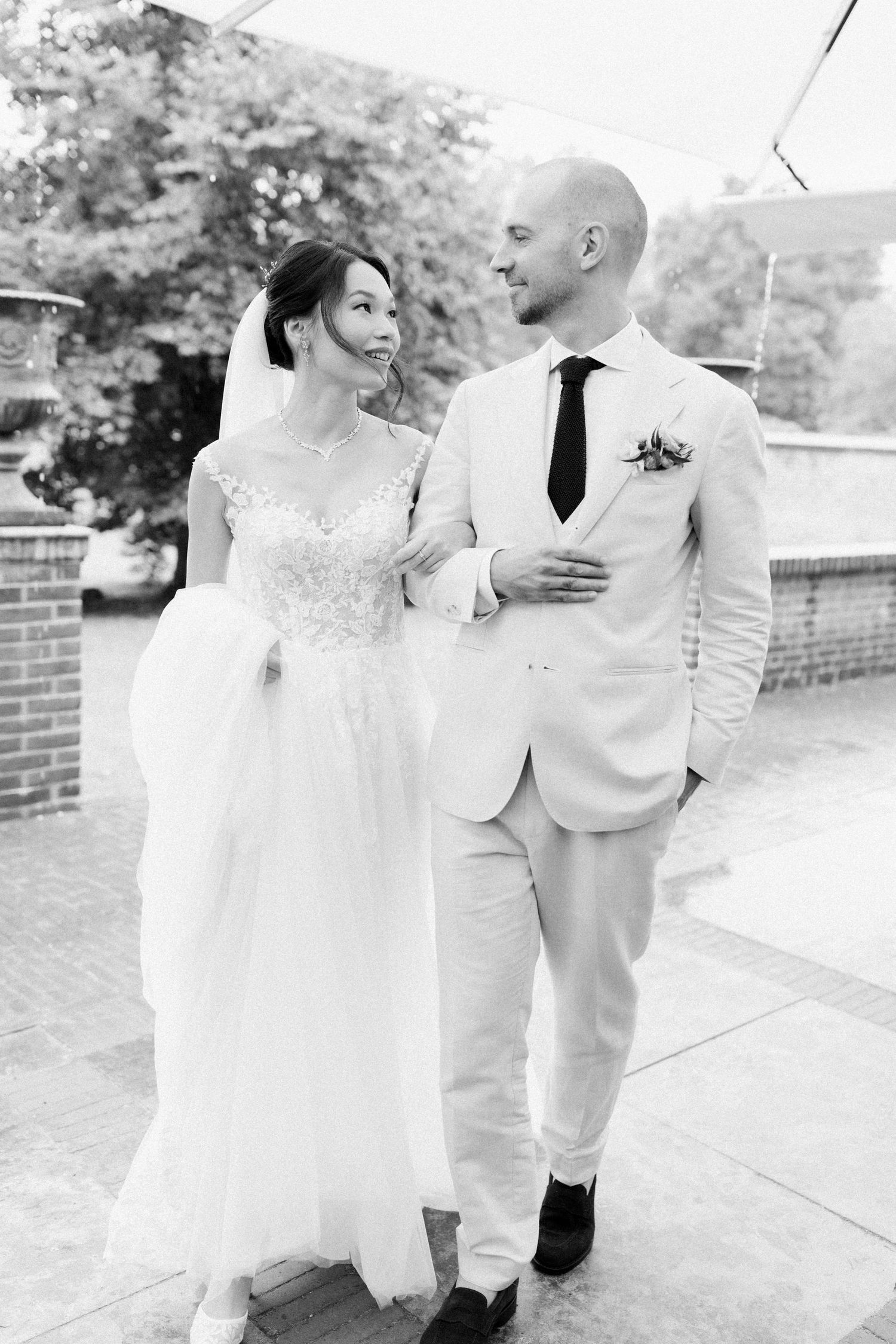 A black and white wedding photograph of a couple in elegant attire sharing a joyful moment outdoors.
