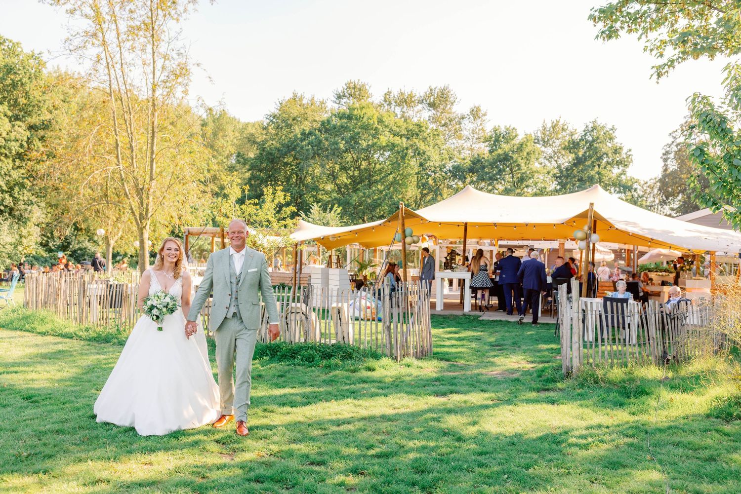 Outdoor wedding reception with rustic tent and wooden fence decorations in a garden setting.