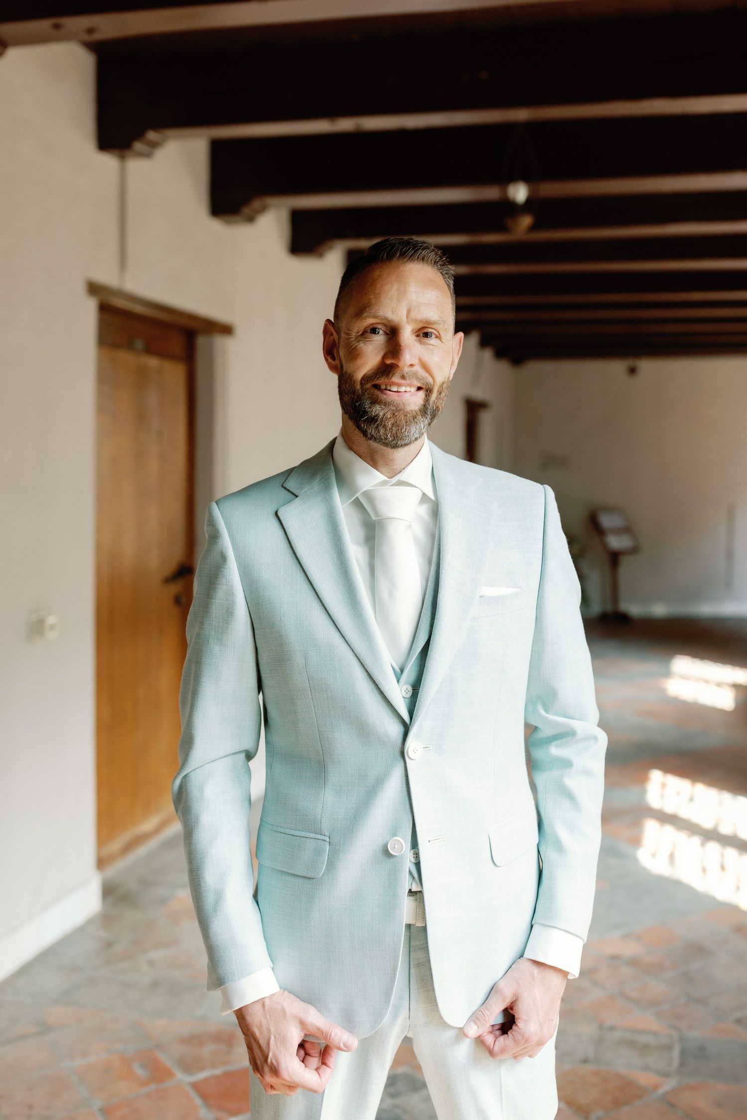 A light mint green suit jacket shown from different angles in a room with exposed wooden beams and white walls.
