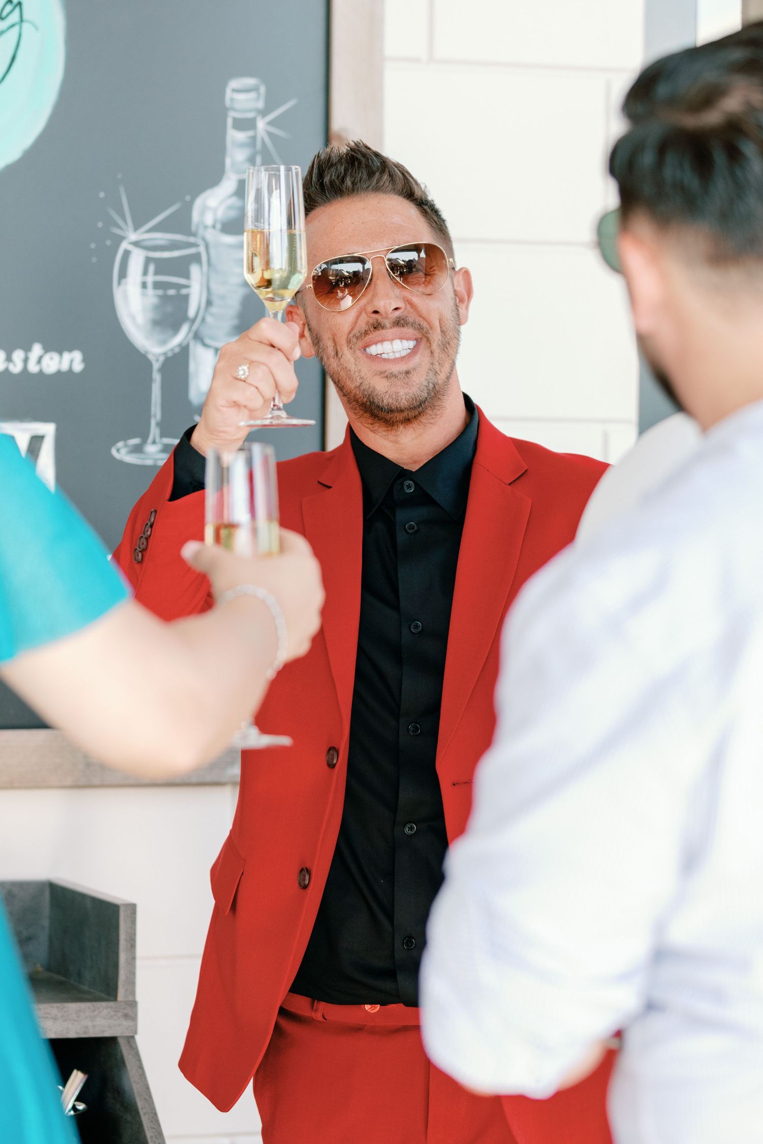 Person in red jacket raises glass during celebratory toast at indoor event.