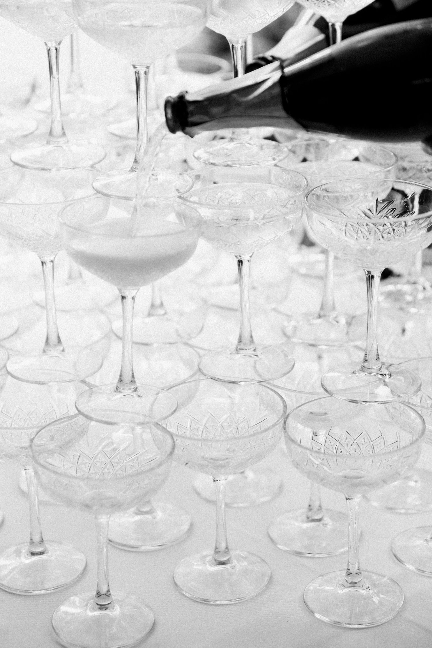 Multiple champagne glasses arranged in rows being filled with sparkling wine at an elegant event.