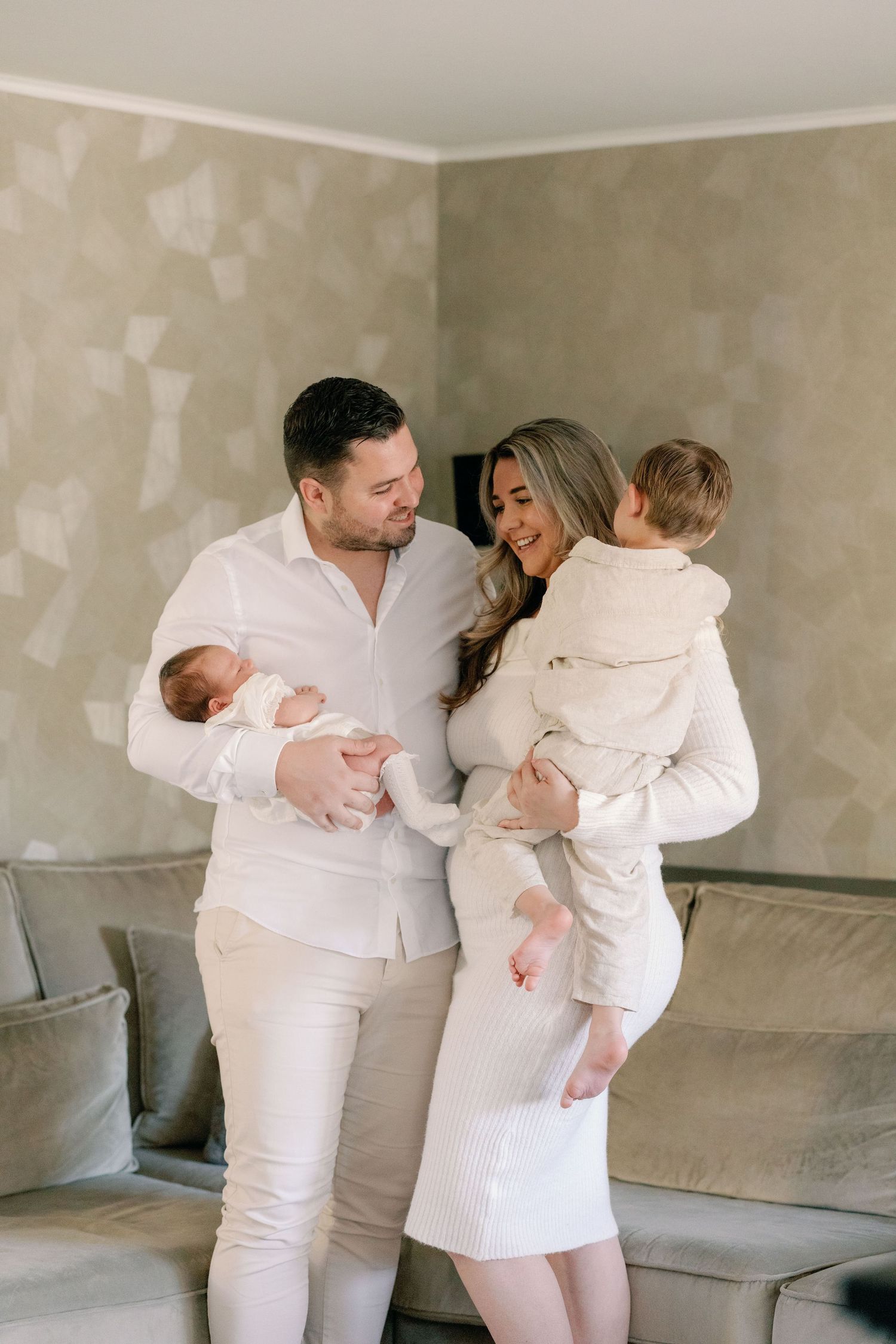 Family in white outfits shares loving moments together on grey couch.