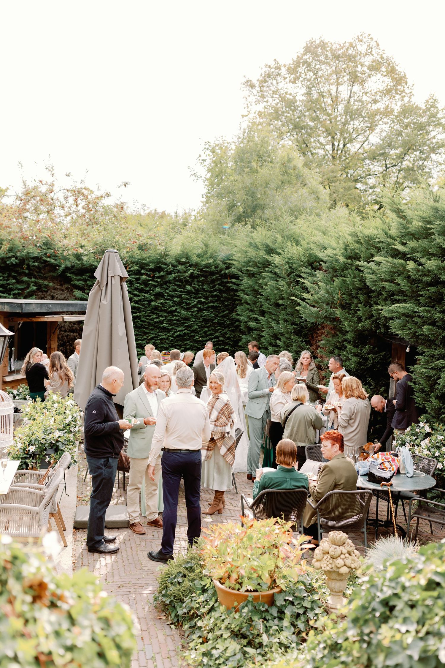 Wedding guests gather on an elegant outdoor patio surrounded by lush greenery for a garden reception celebration.