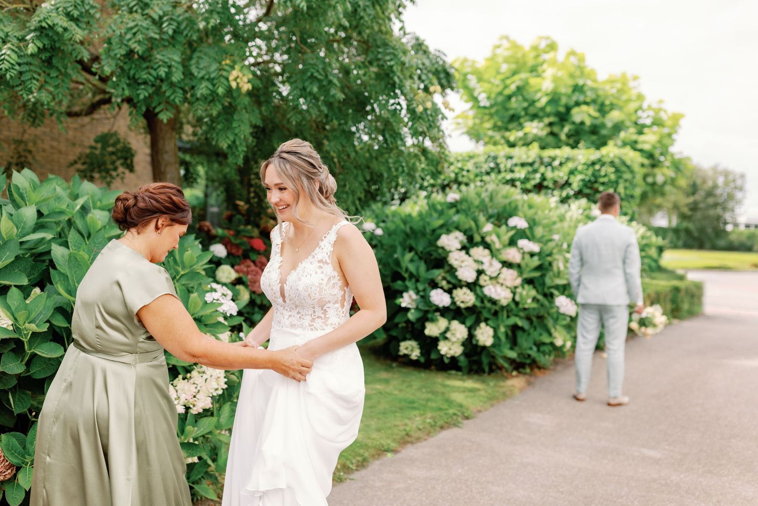 A wedding party walks along a garden path surrounded by lush greenery and blooming hydrangea bushes.