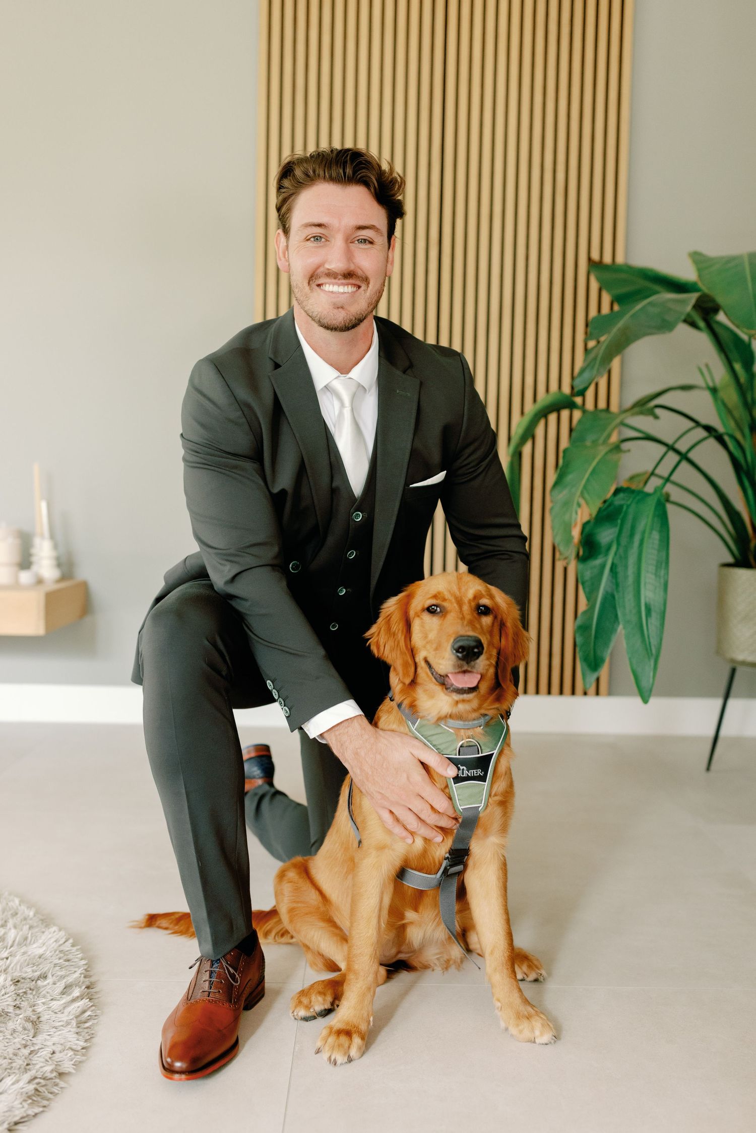 A person in a dark suit sits and poses with an adorable golden retriever puppy in a modern minimalist setting.