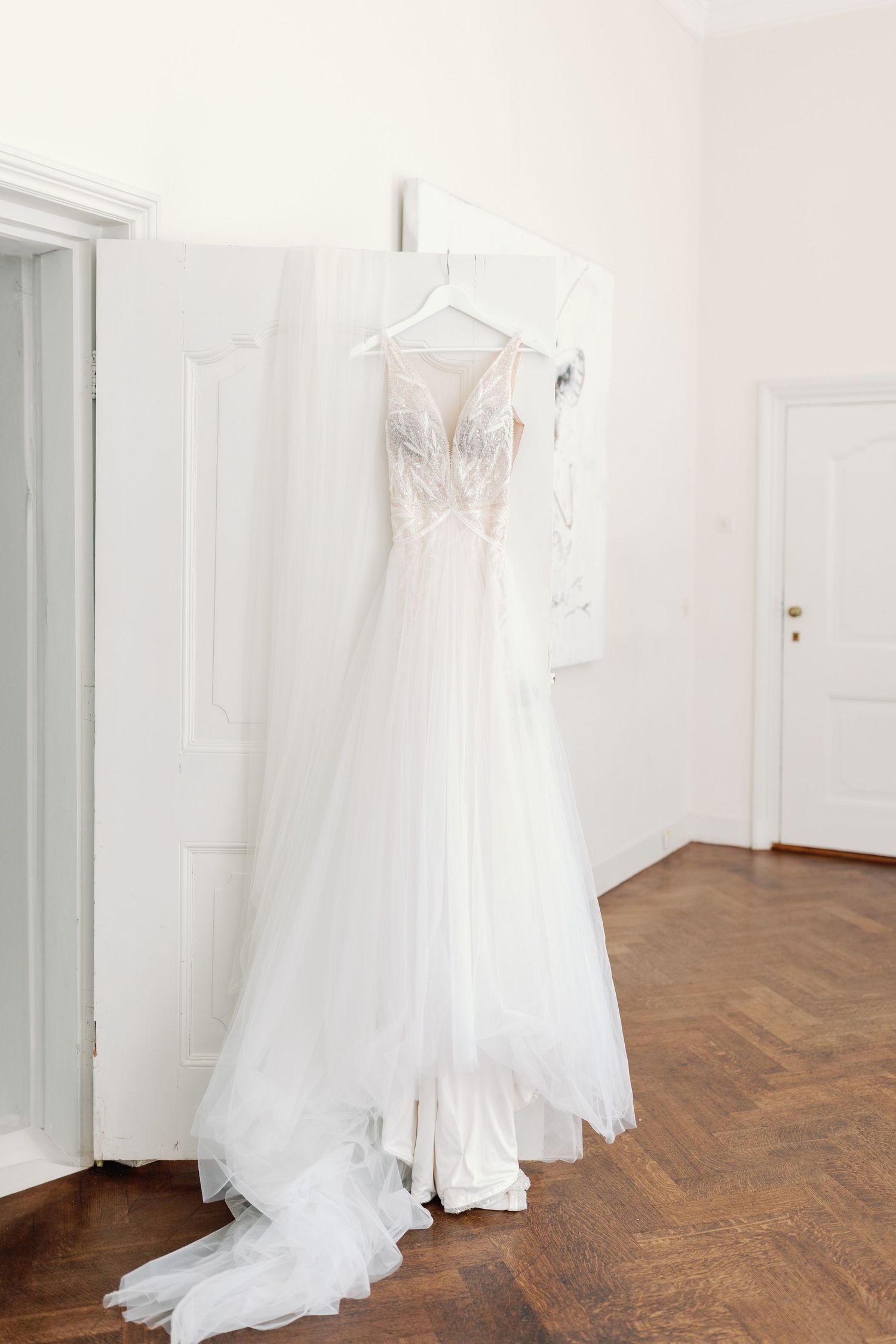 Elegant white wedding dresses displayed in a bright room with hardwood floors and white walls.