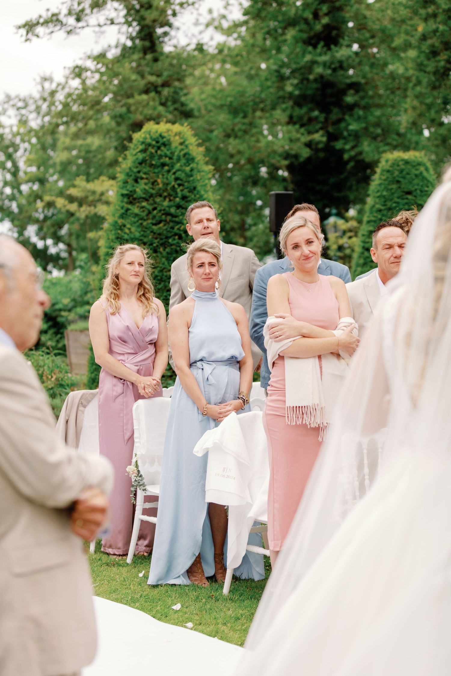 Wedding guests react with joy and emotion during an outdoor ceremony in a garden setting.