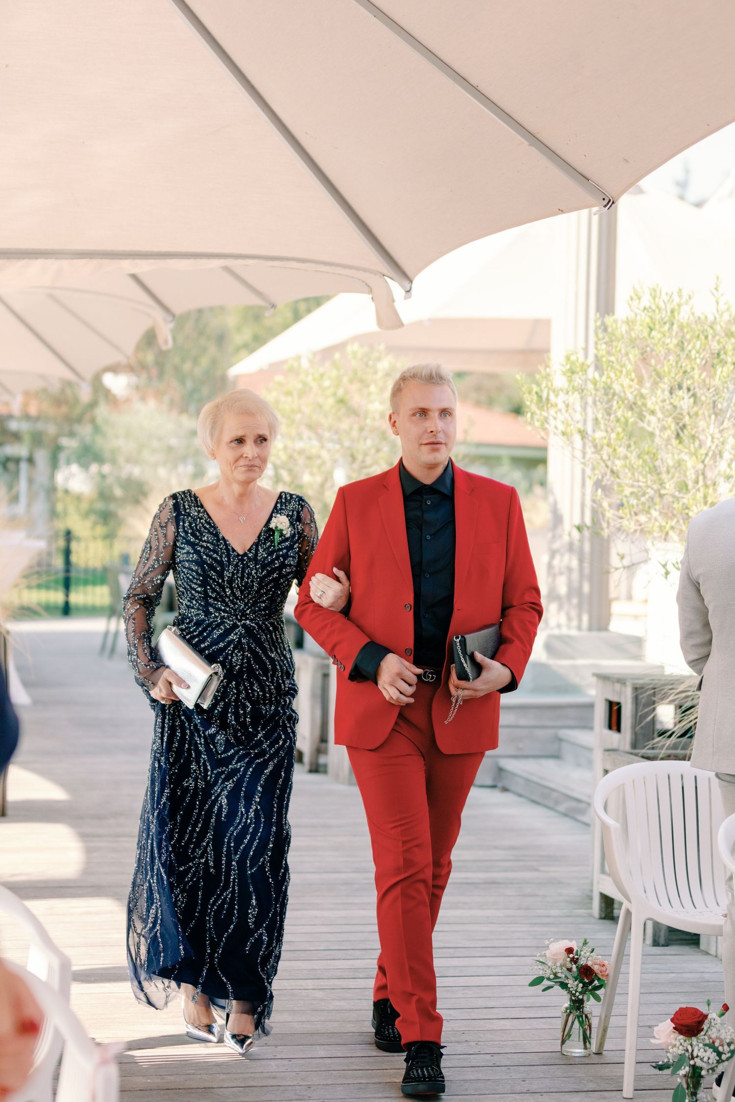Wedding guests in formal wear walking down a covered deck pathway.