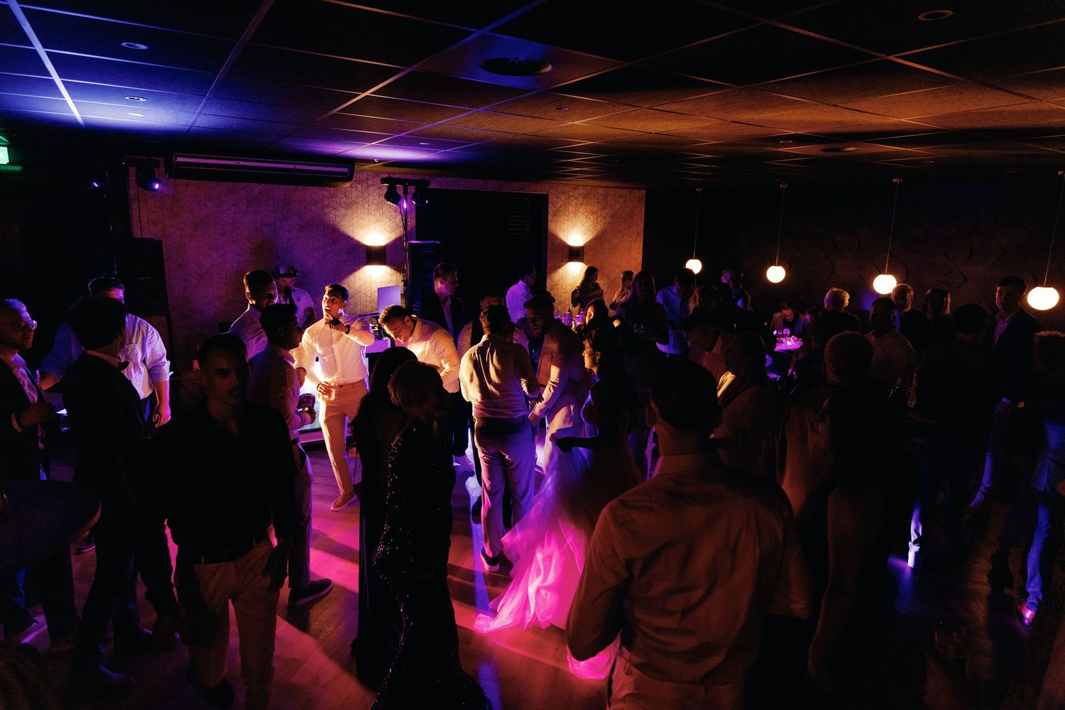 Wedding guests dance under atmospheric lighting at an indoor reception venue.