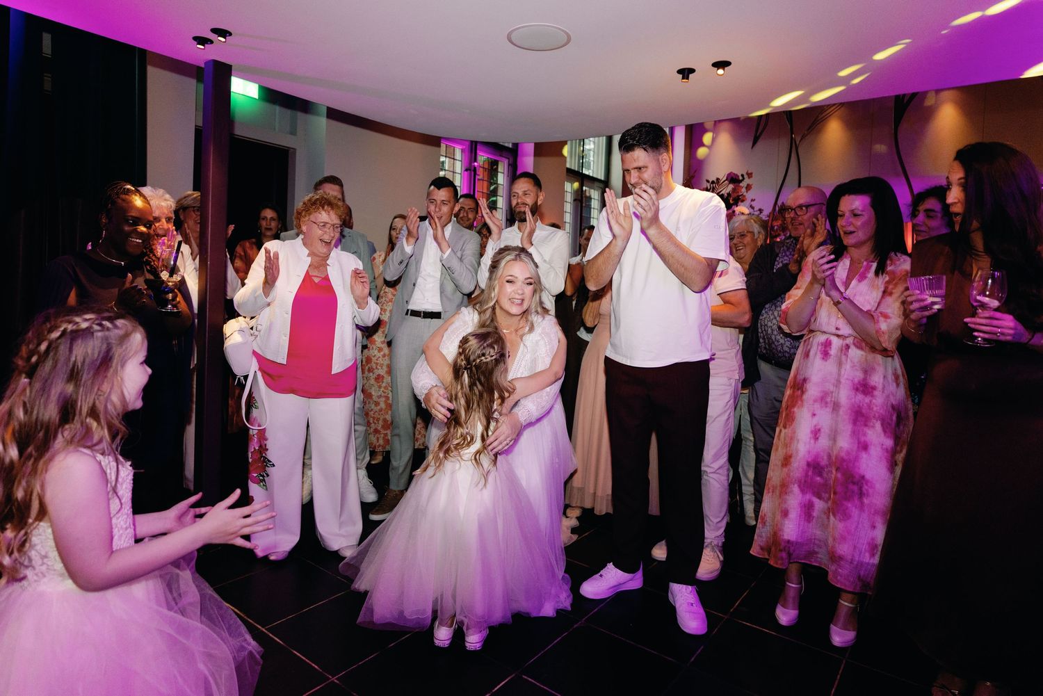 Wedding guests dance and celebrate on a purple-lit dance floor during an evening reception celebration.
