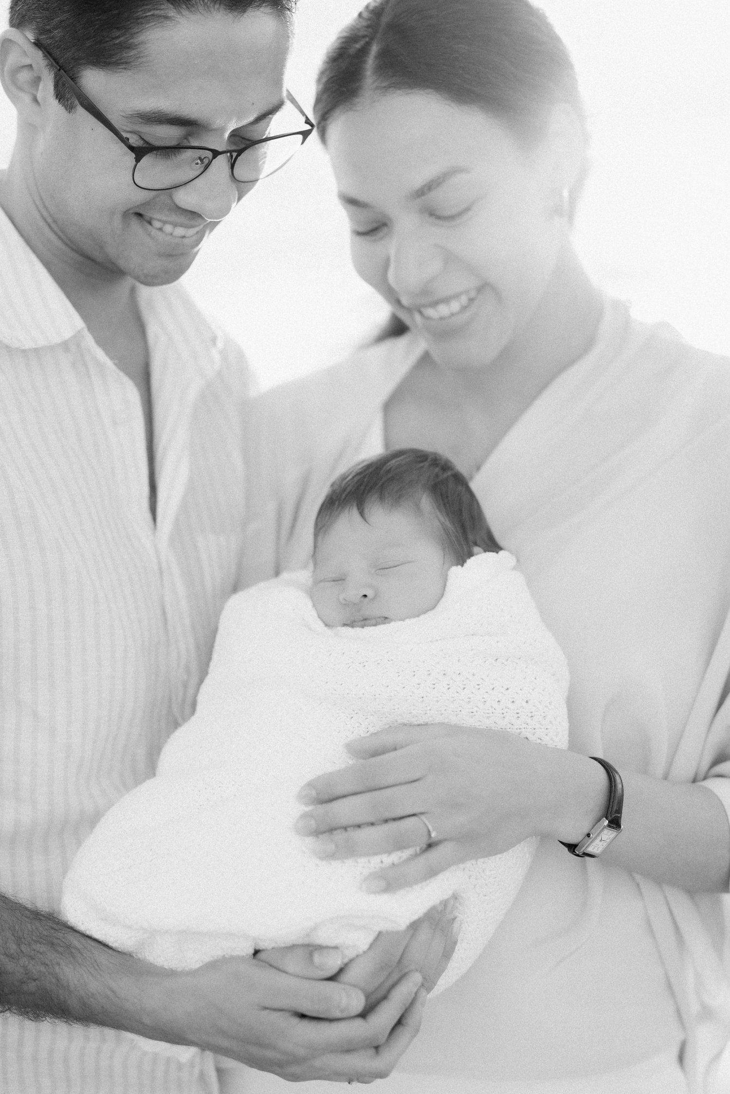 Family shares intimate moment with newborn baby in bright white studio.