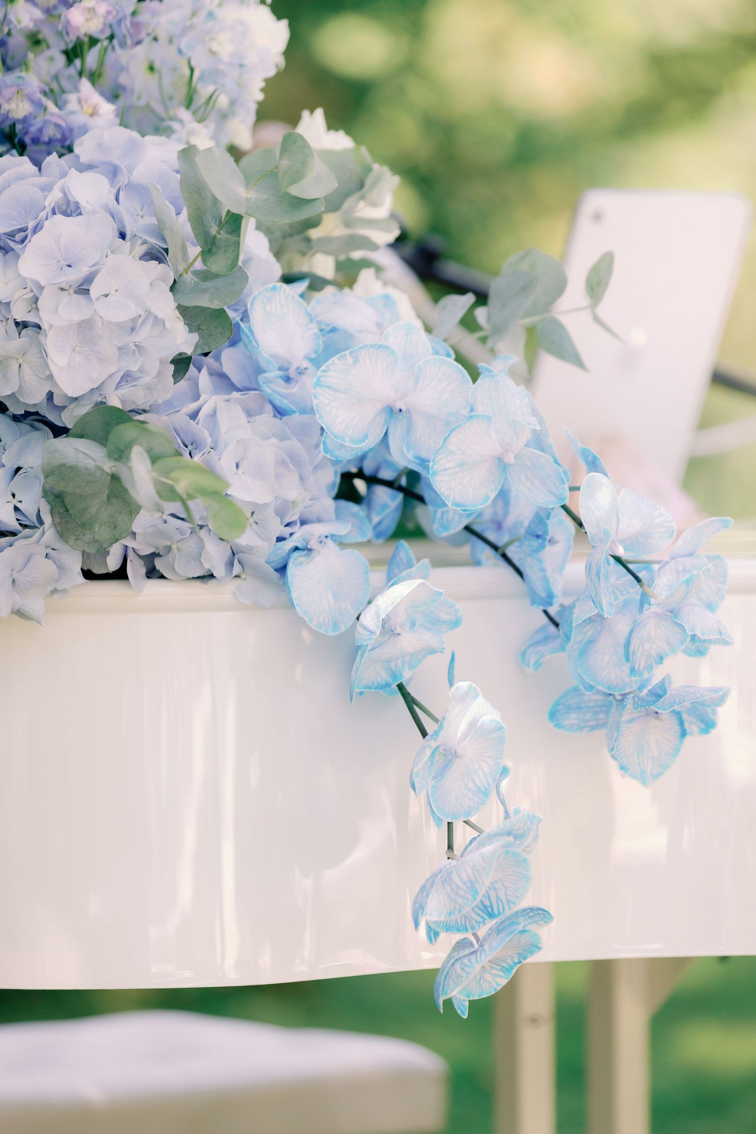 Blue hydrangeas and orchids cascade over a white surface at an elegant outdoor wedding decoration.