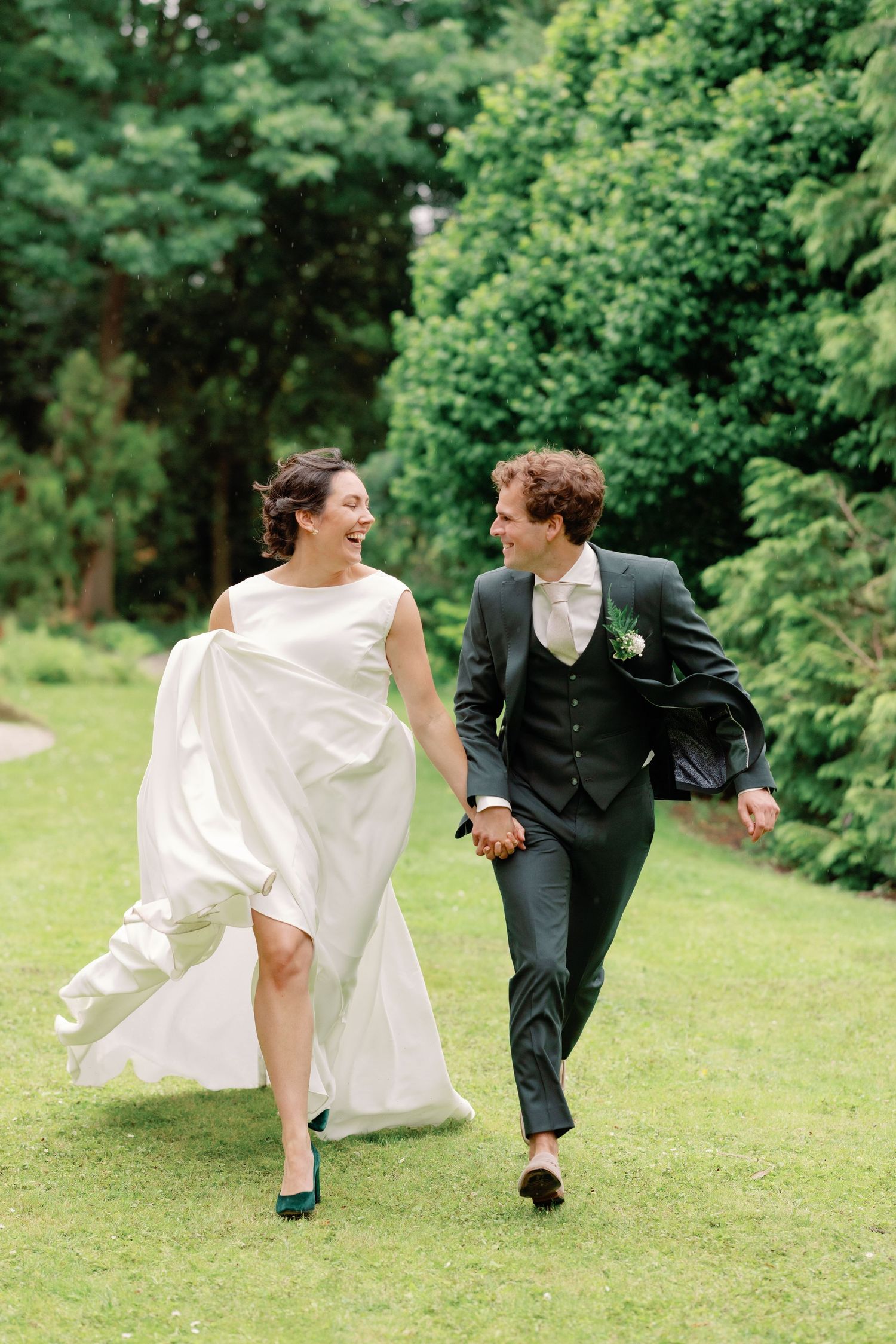 Joyful couple runs hand-in-hand across a lush green lawn, with the bride's white dress flowing in the breeze.