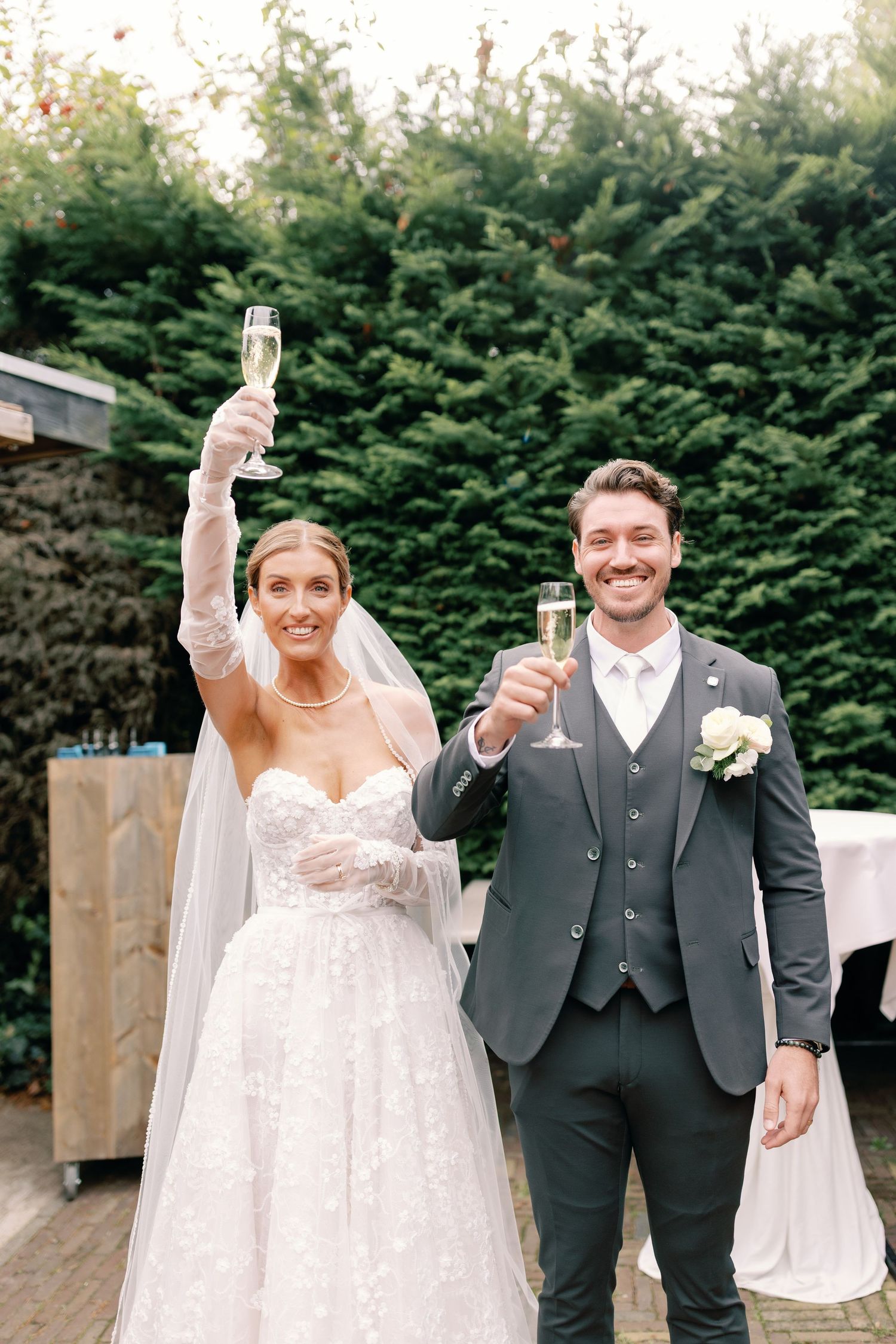 A bride and groom celebrate their wedding day with champagne toasts outdoors.