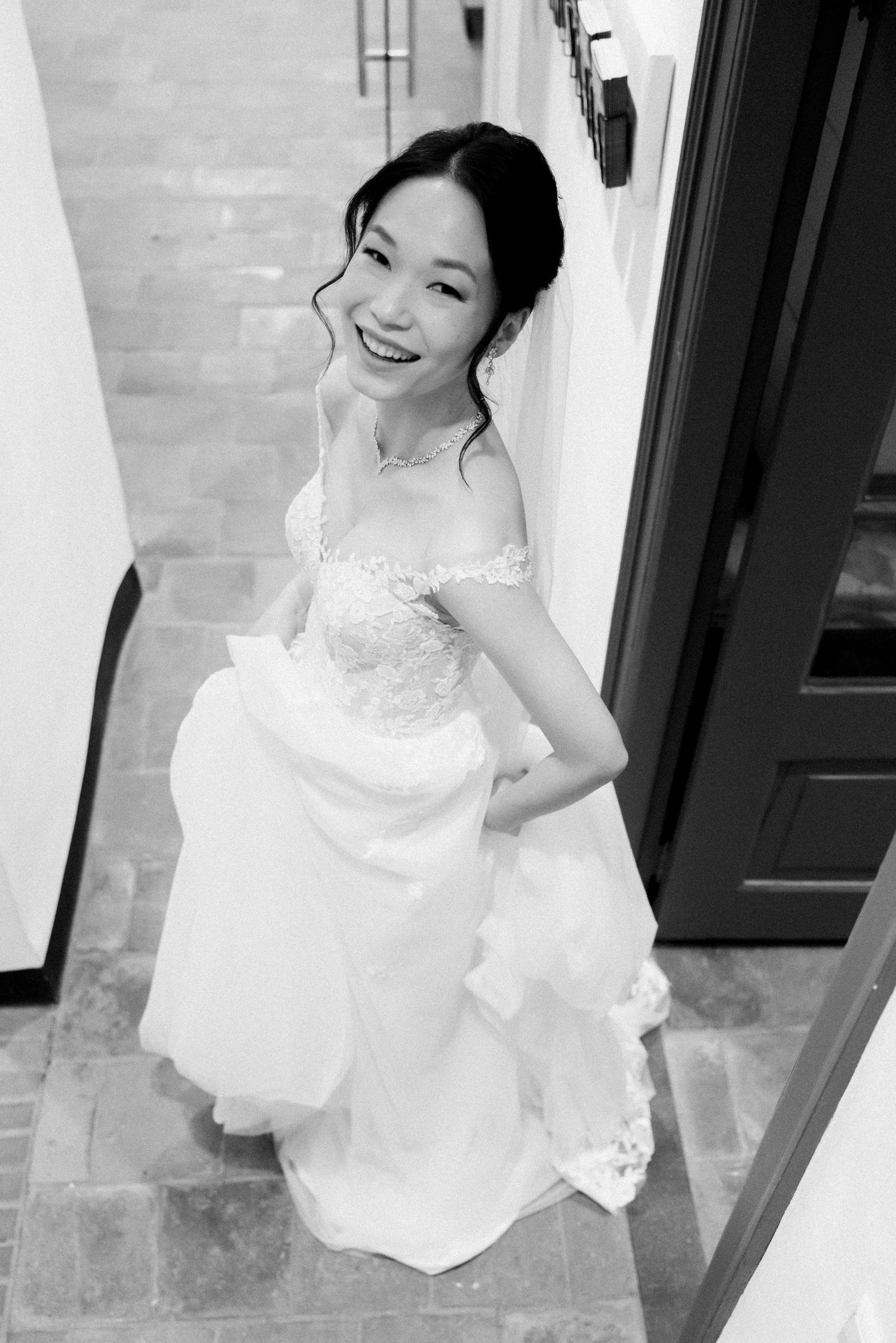 Black and white photos of a joyful bride in a white lace dress posing against a brick wall.