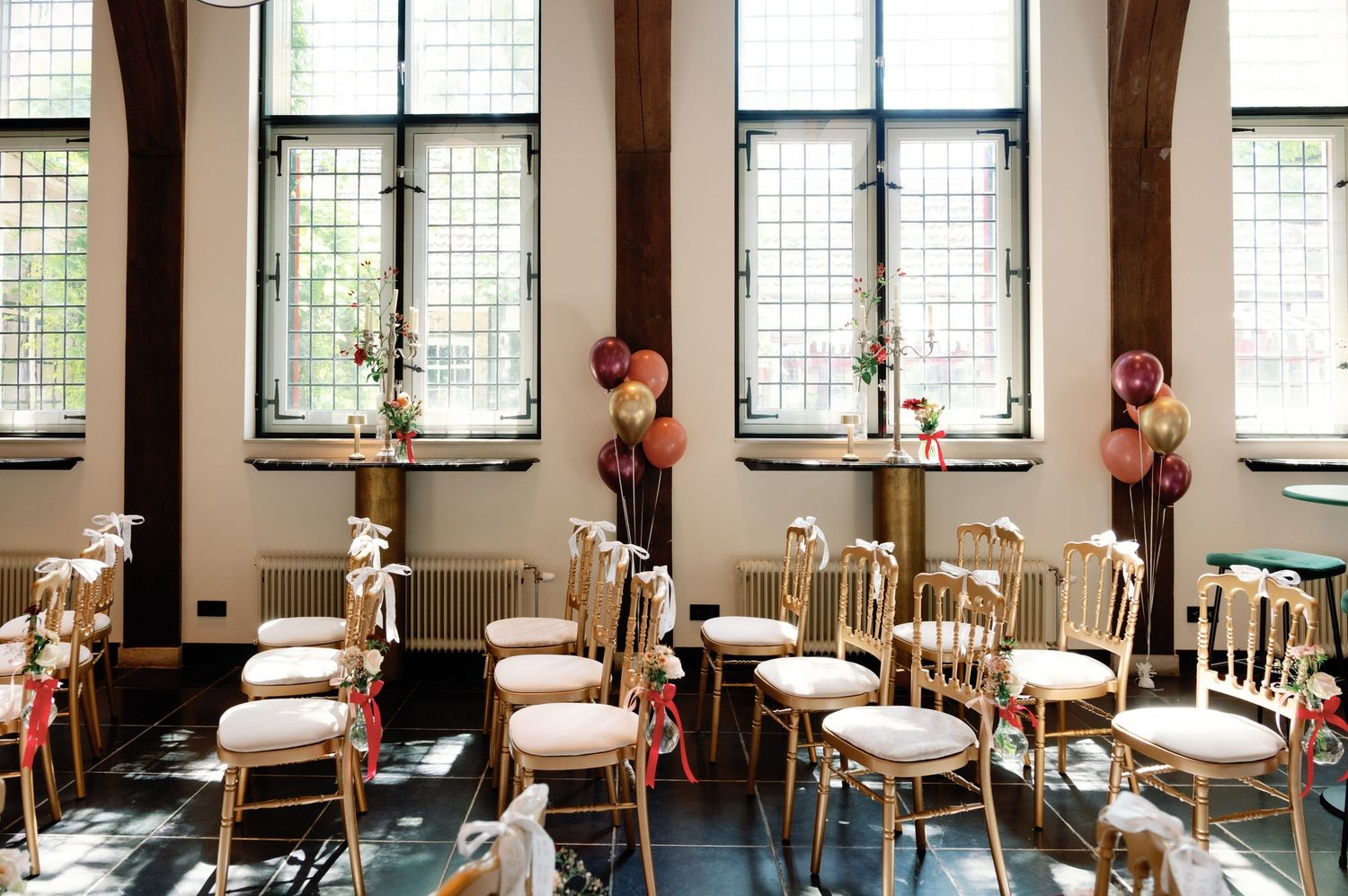 Wedding ceremony venue with tall windows, vintage chairs, and floral arrangements in an elegant church setting.