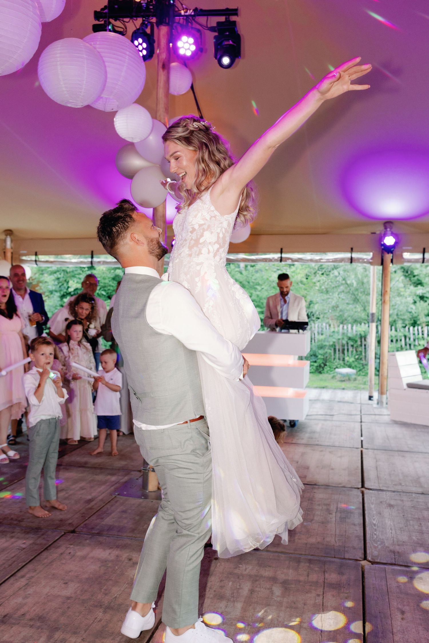 Newlyweds share a joyful dance moment under purple lighting and white paper lanterns at their wedding reception.