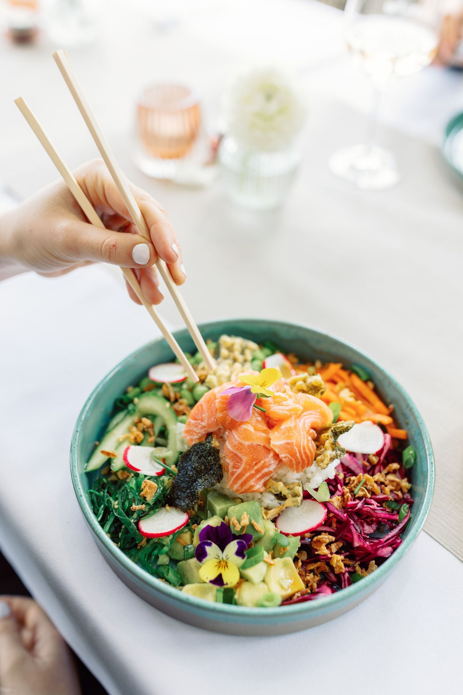 Vibrant poke bowl with fresh salmon, colorful vegetables, and garnishes served in a turquoise ceramic bowl.