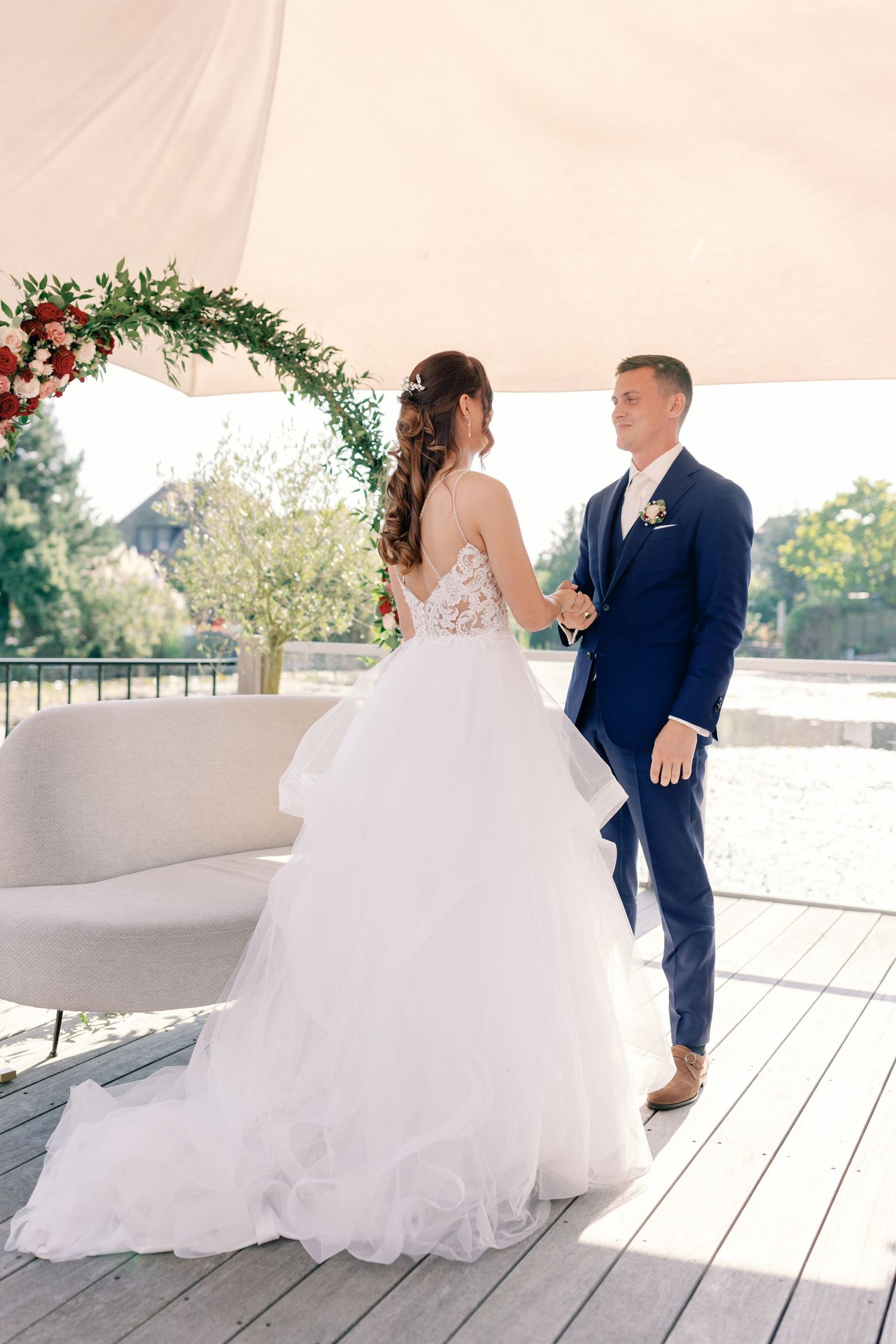 A couple shares a moment under a floral arch at their outdoor wedding ceremony, with the bride in a flowing white gown.