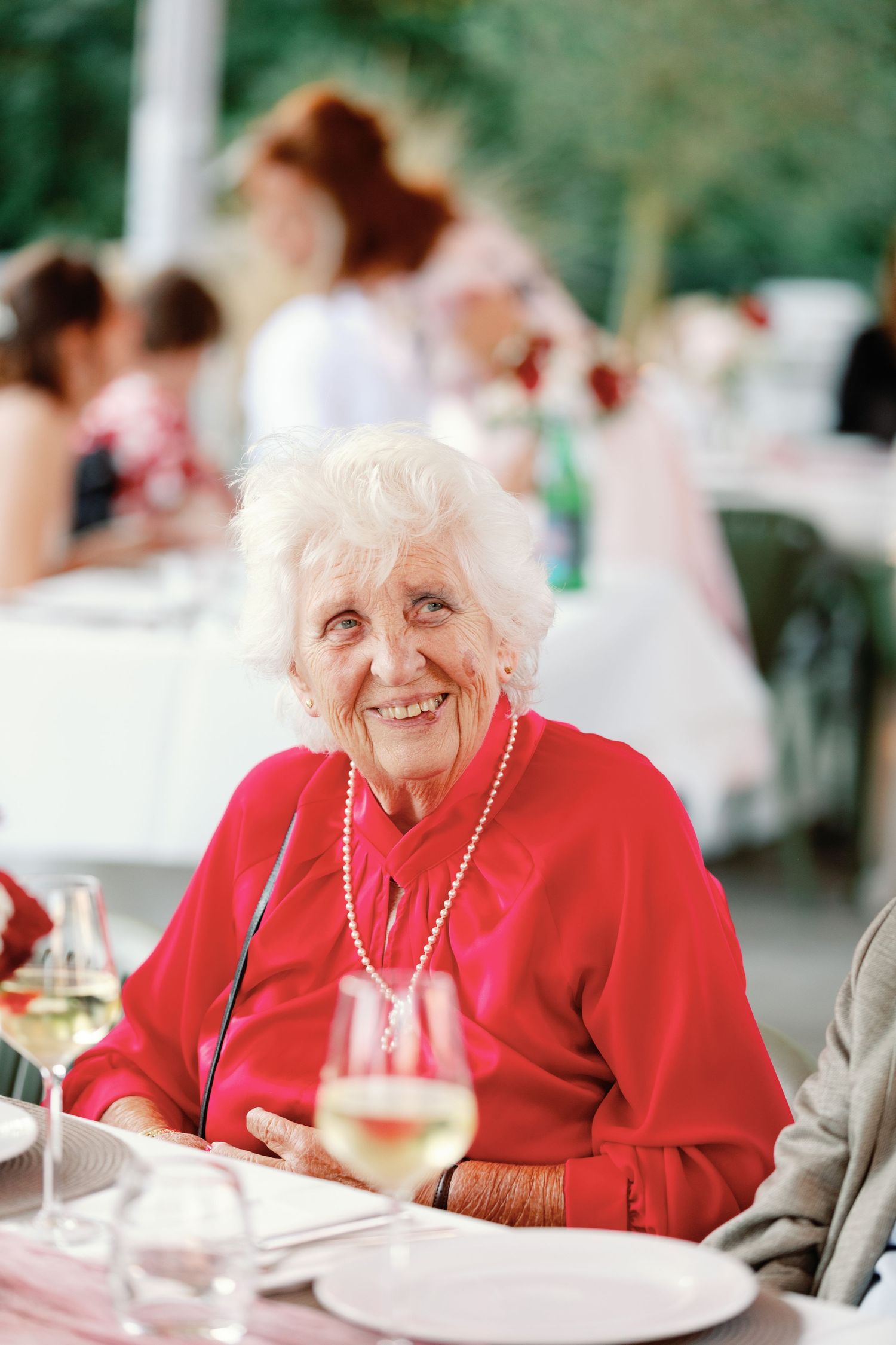 Guest in bright red attire enjoying wine at an outdoor celebration.