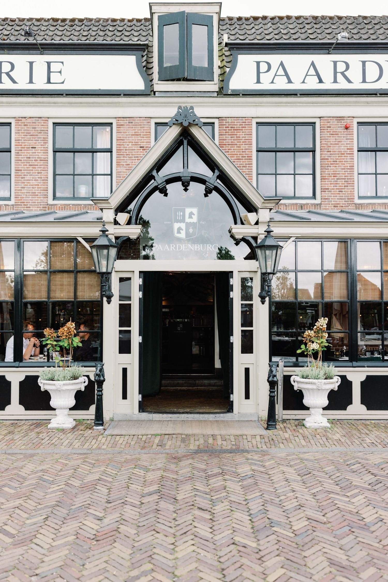 Brick storefront with traditional Dutch architecture featuring black trim and cobblestone street in a historic shopping district.