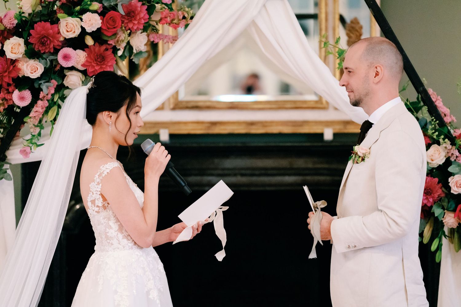 Couple shares intimate first dance under floral arch during elegant indoor wedding ceremony.