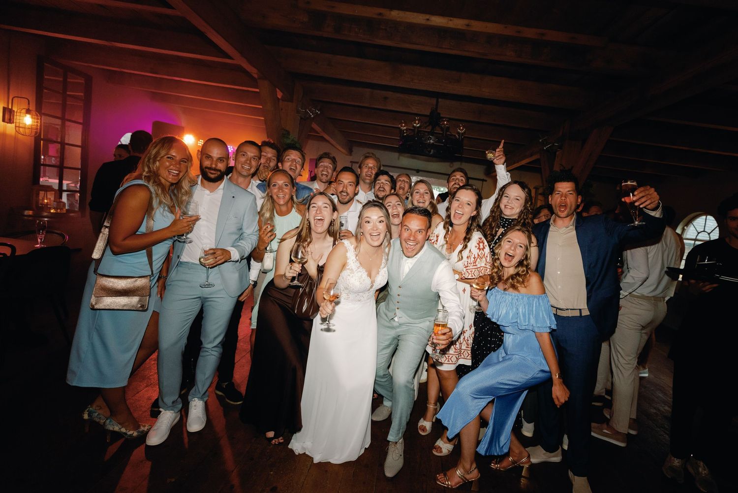 Wedding guests dance and celebrate together on a dimly lit dance floor during an evening reception celebration.