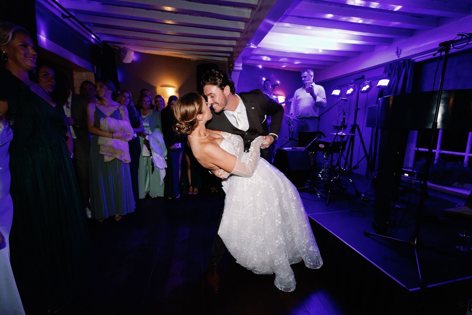 Wedding guests dance under vibrant purple lighting on a dance floor during an evening reception celebration.