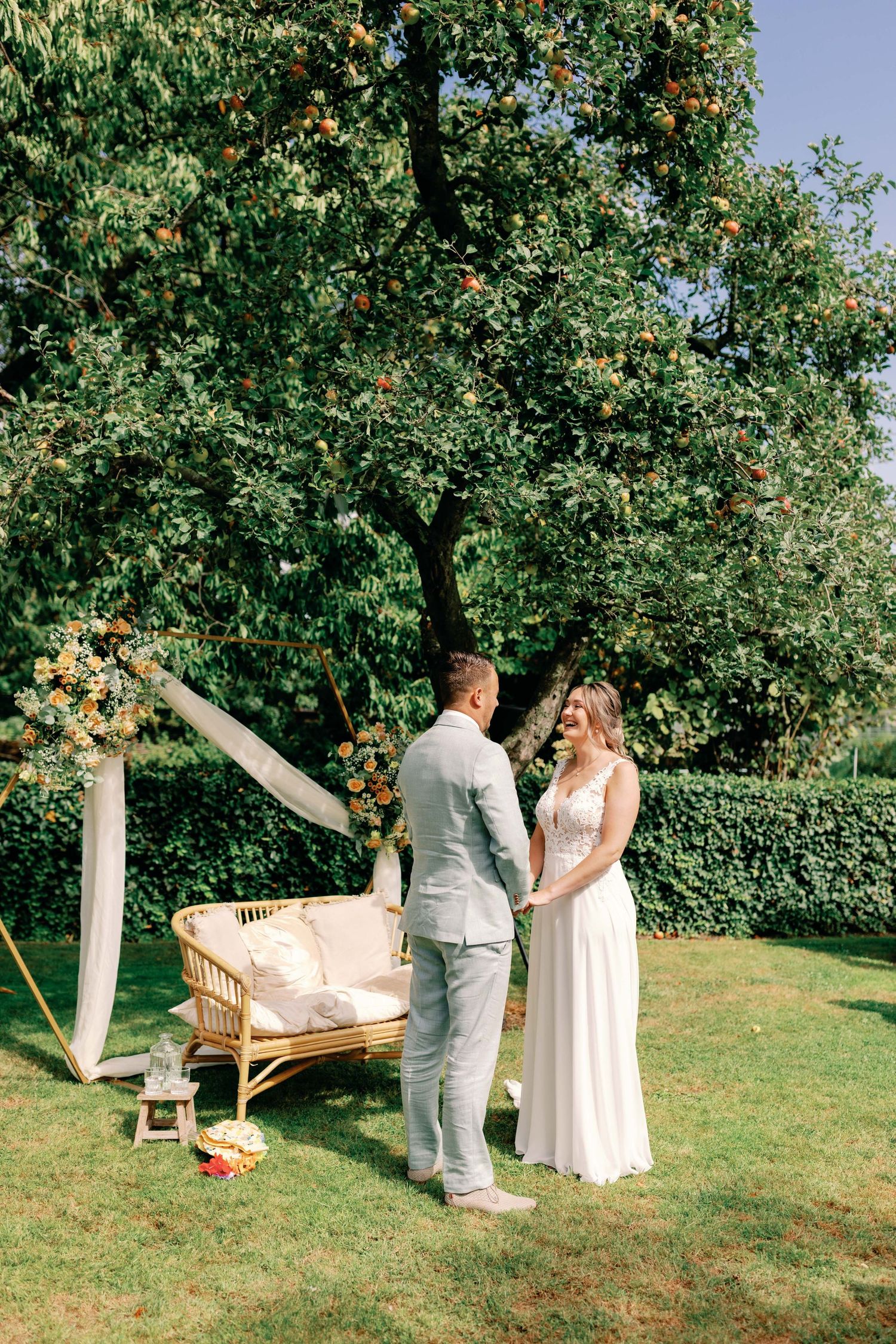 Romantic outdoor wedding ceremony in an apple orchard with white draping and rustic wooden seating.