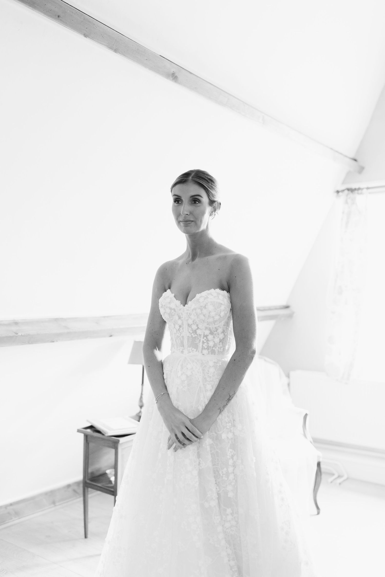 Black and white photograph showing a bride in a strapless lace wedding gown in a bright, minimalist setting.