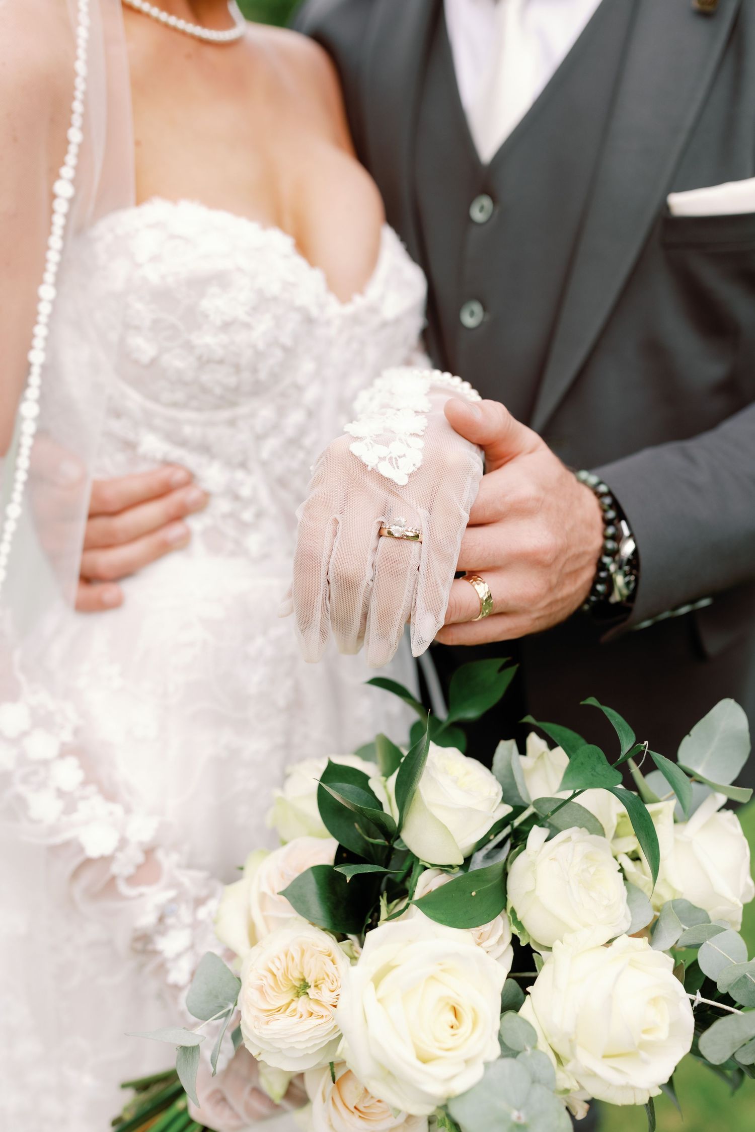 Close-up detail of a white lace wedding dress and elegant ivory rose bouquet with eucalyptus greenery.