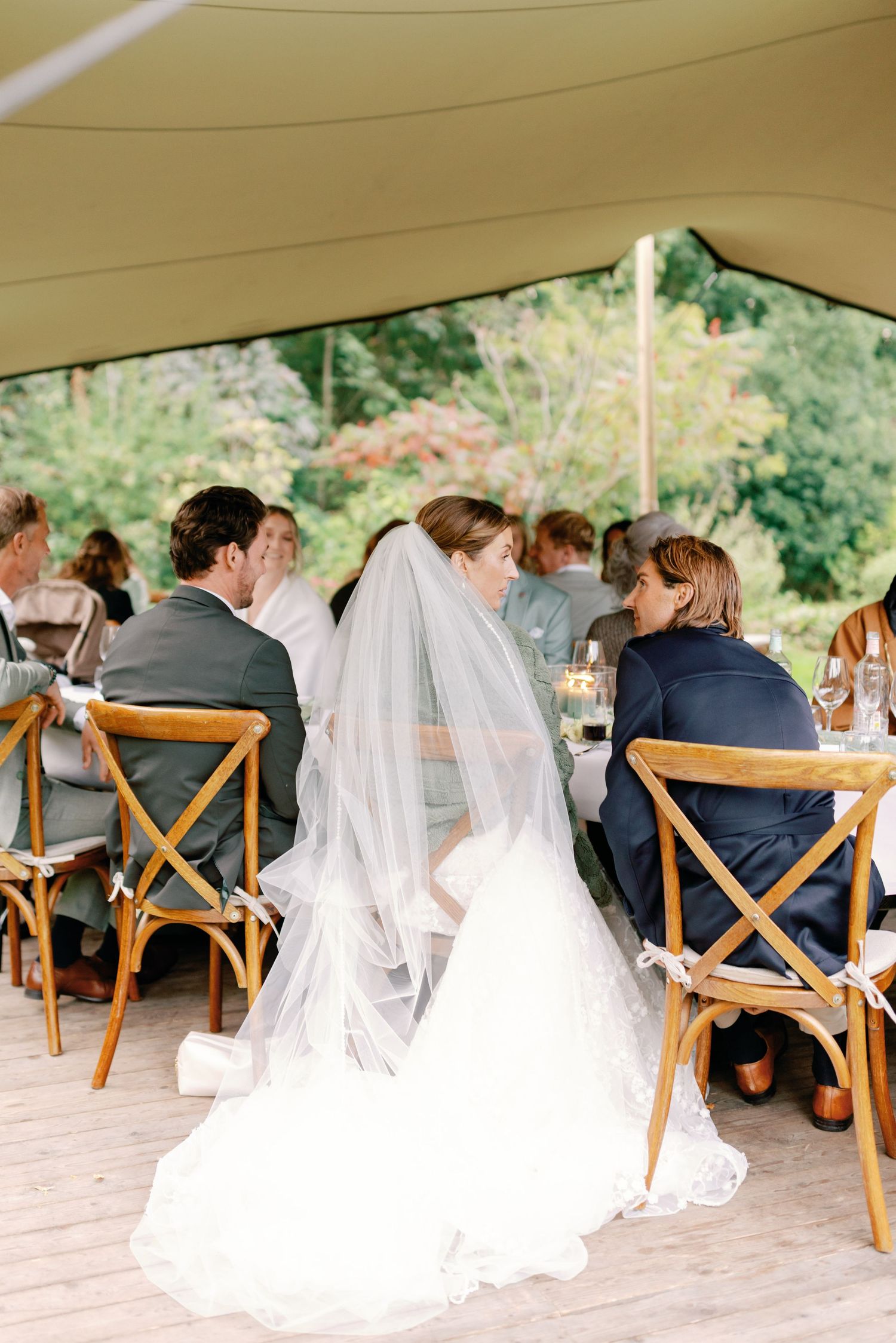 A panoramic sequence of wedding guests seated in wooden cross-back chairs under a tent during an outdoor ceremony.