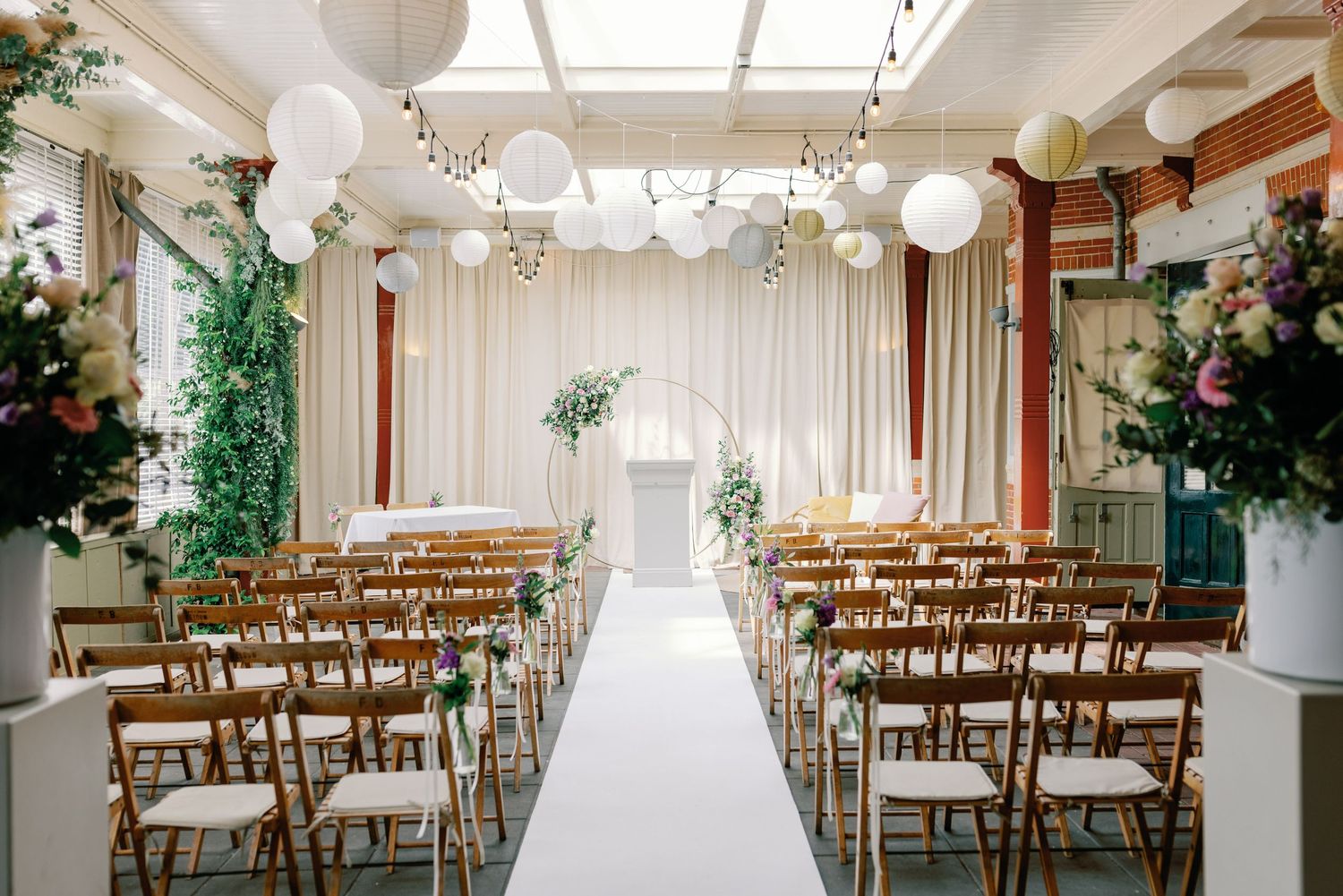 Light-filled wedding ceremony space with wooden chairs and floral decorations.