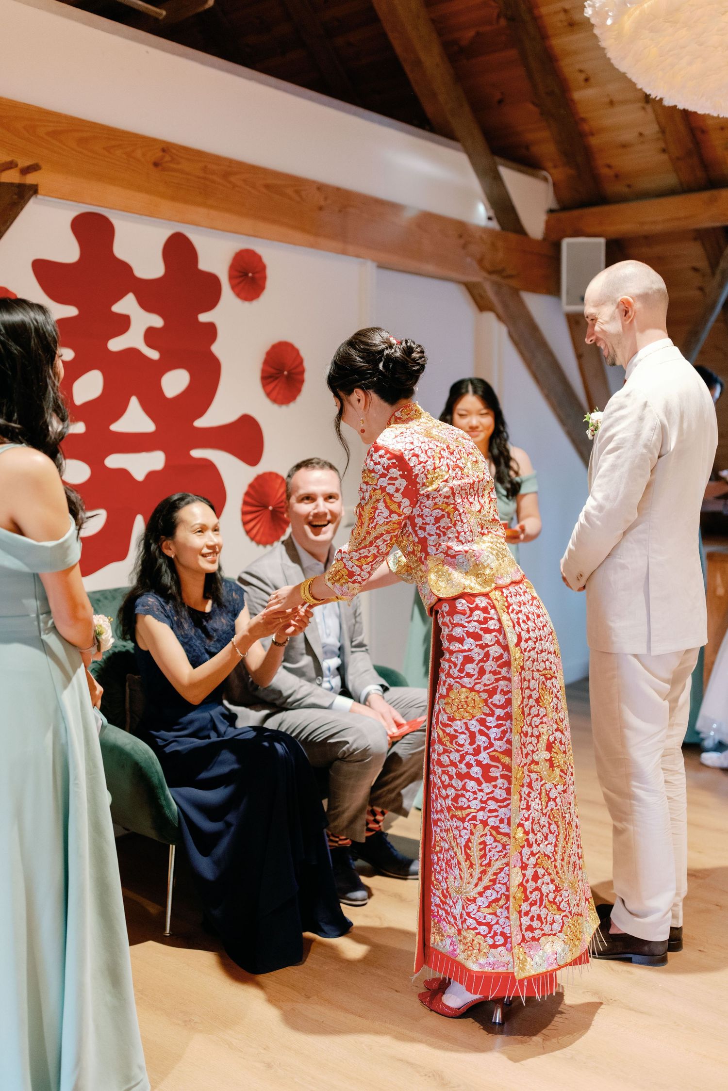 People gathered in a room wearing traditional dress and formal attire engage in a celebratory social event.