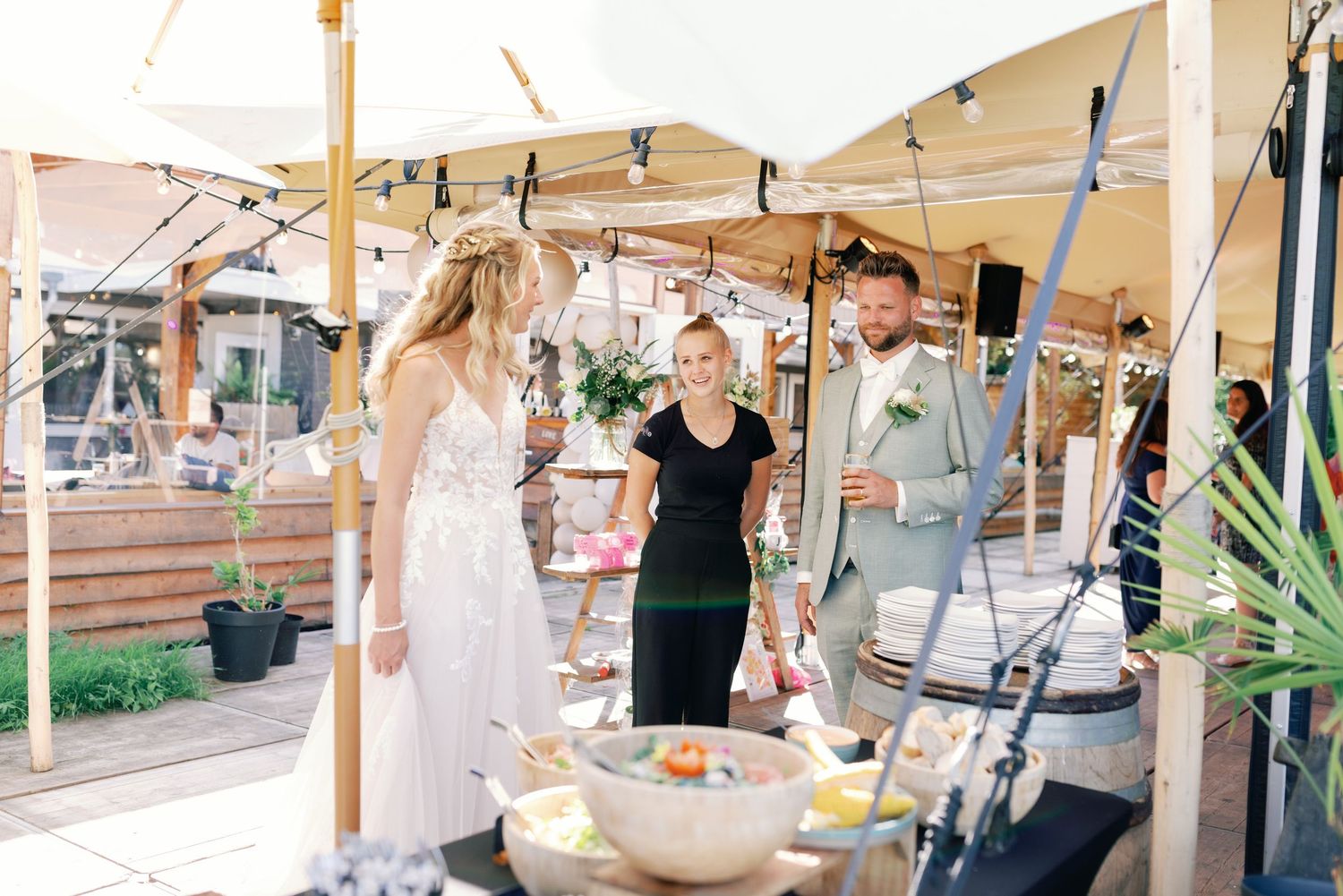 A festive outdoor event space decorated with string lights and white canopies where people gather for a celebration.